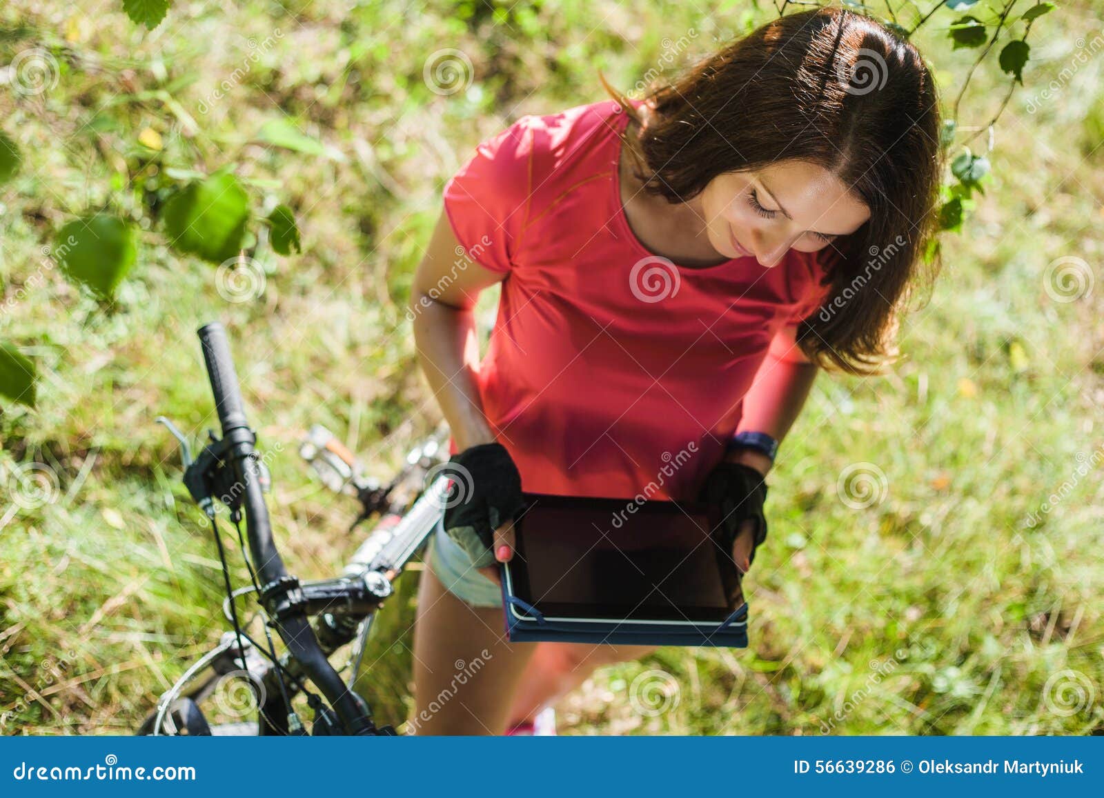 Muchacha del deporte en la tableta digital del control de la bicicleta. Muchacha sonriente del deporte en la tableta digital del control de la bicicleta al aire libre