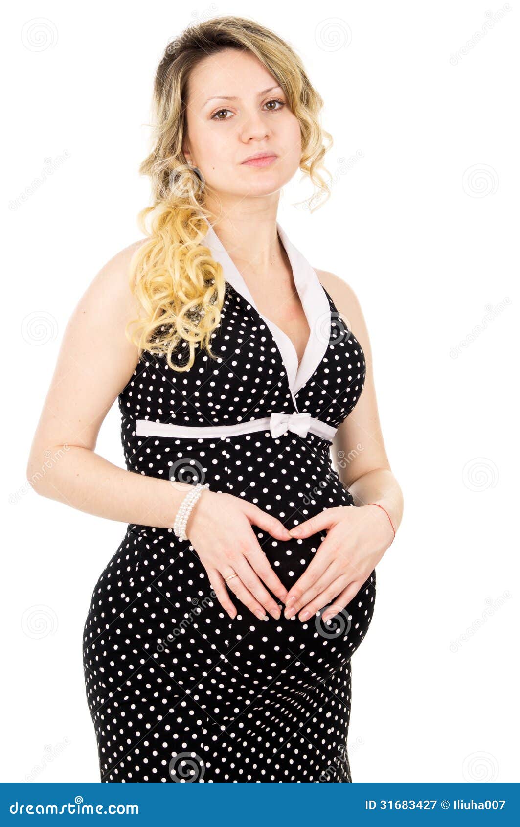 La muchacha embarazada hermosa en un vestido en el abdomen muestra el corazón