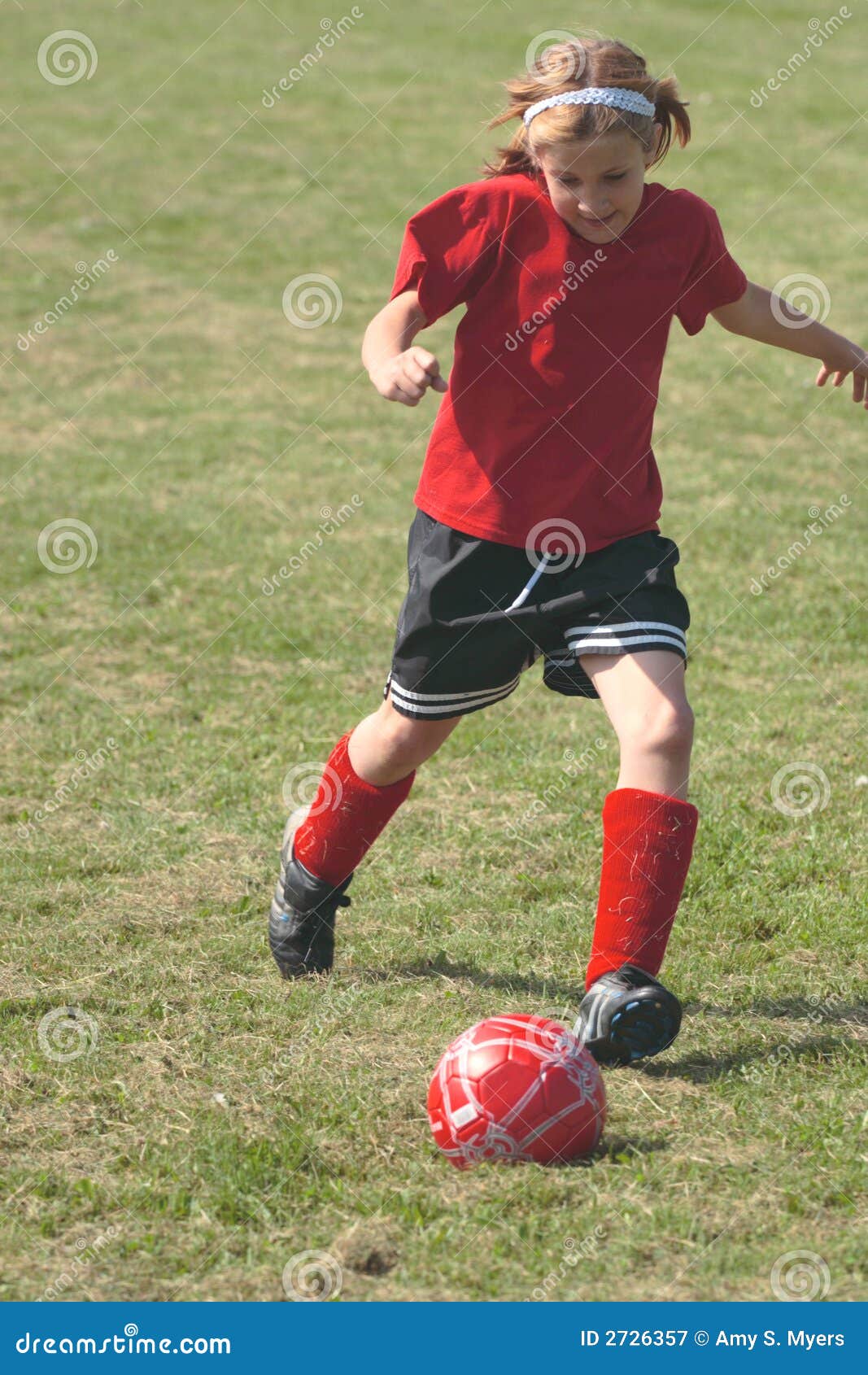 Muchacha en el campo de fútbol 1B. Muchacha que golpea el campo de fútbol de la bola con el pie abajo durante juego.