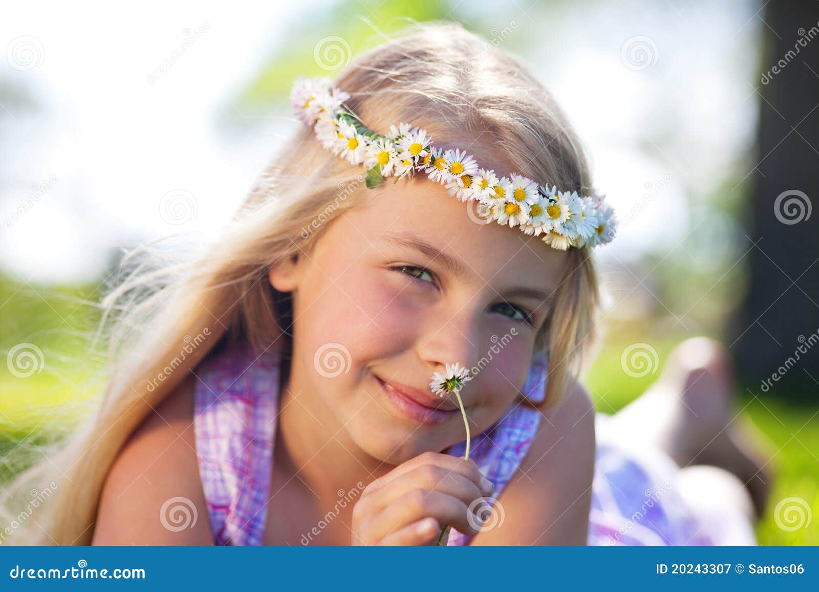 Muchacha ideal del verano. Niña que miente en la hierba con las flores alrededor de su cabeza y olores en una margarita