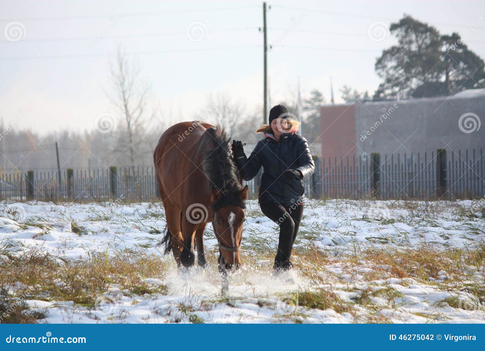 Muchacha rubia del adolescente y caballo marrón que corren en la nieve en el campo