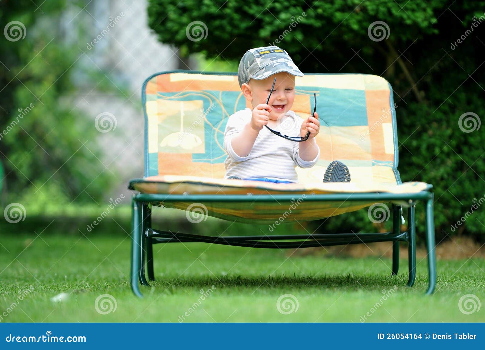 Muchacho en casquillo. Bebé en el casquillo lounging en silla con las gafas de sol