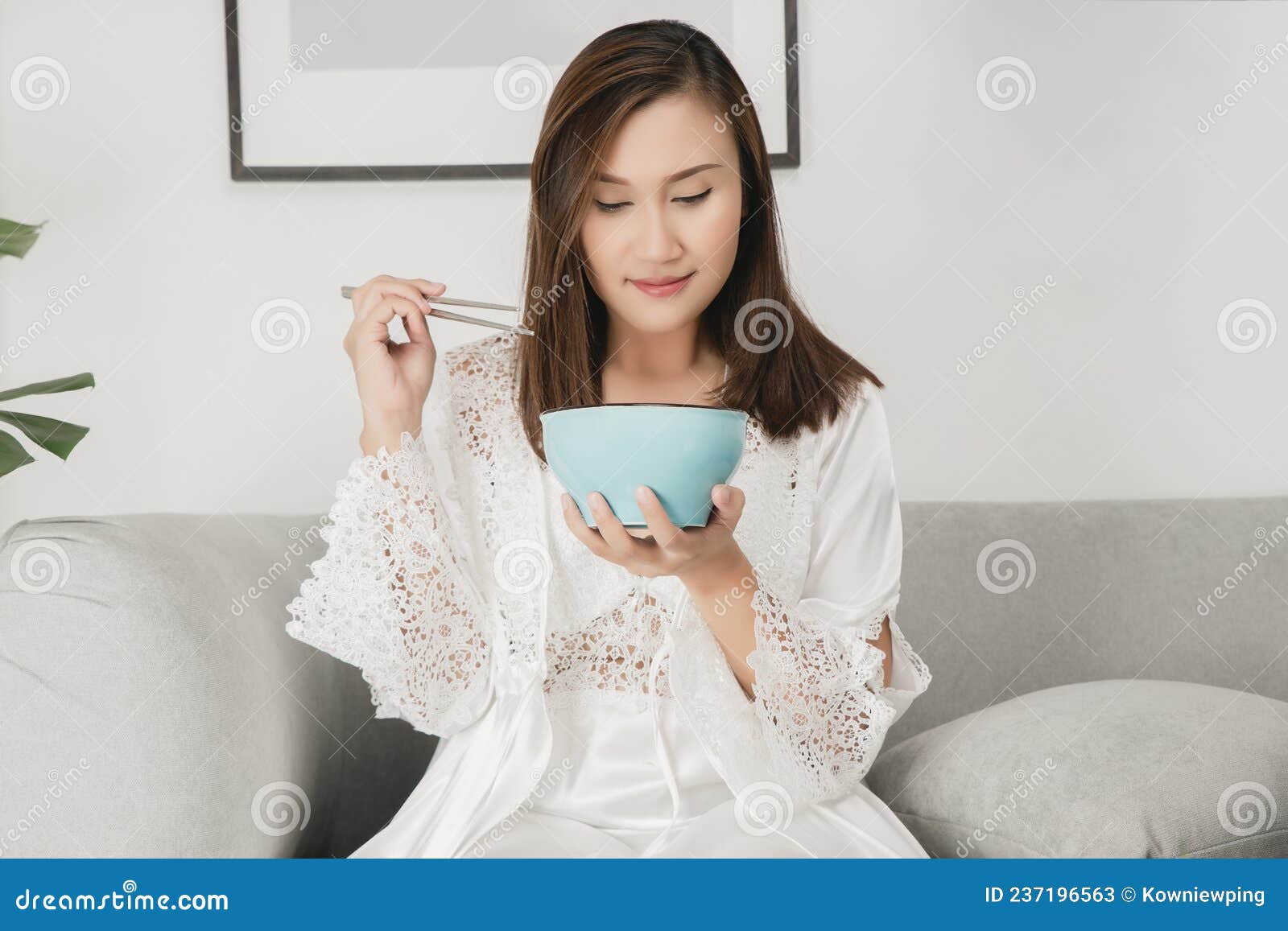 Mujer Asiática Con Camisón De Satén Blanco Sentada En Un Sofá Gris Y  Comiendo Comida Durante La Noche Imagen de archivo - Imagen de muchacha,  tenencia: 237196563