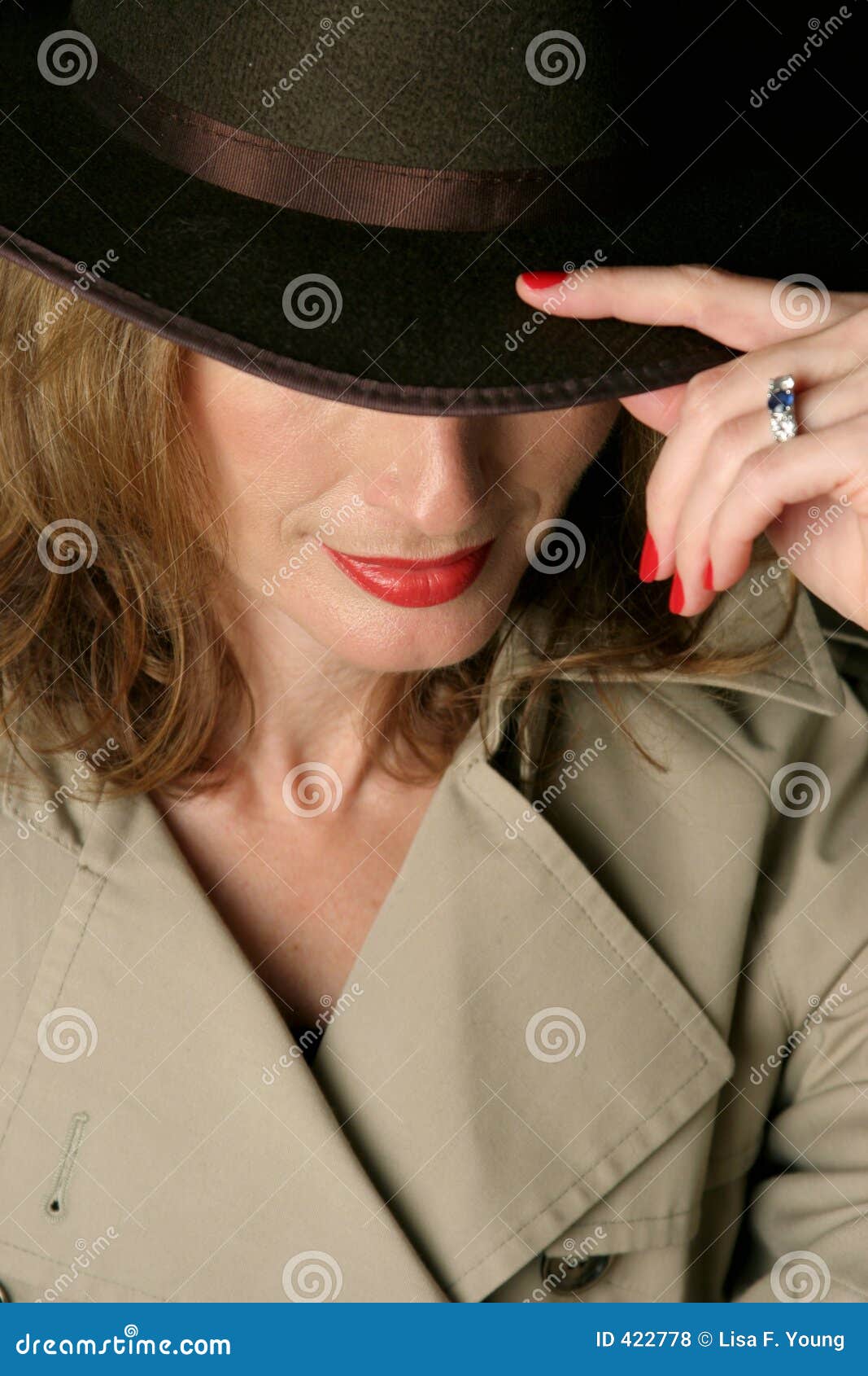 Mujer atractiva de Trenchcoat. Una mujer en un trenchcoat y un sombrero hermosos, atractivos del sombrero de ala. La los ojos encubren debajo del borde del sombrero.