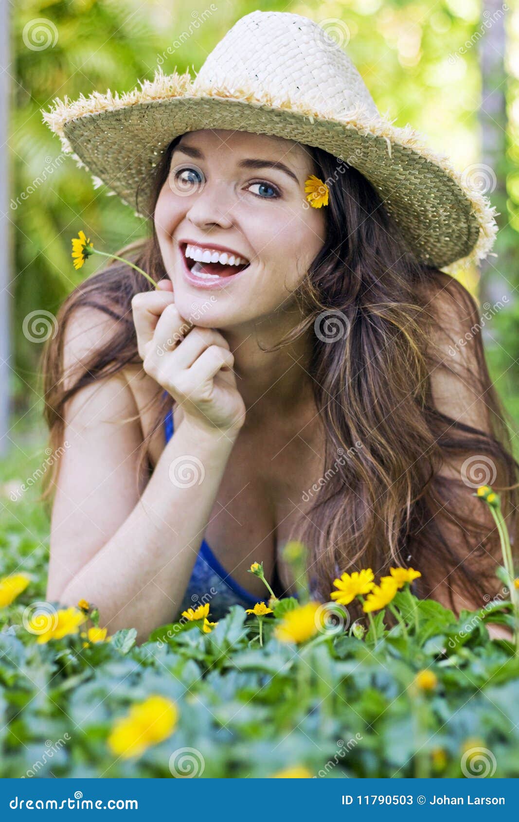 Mujer atractiva en sombrero y flores. Muchacha hermosa que miente en la hierba que sonríe con las flores amarillas que desgastan un sombrero