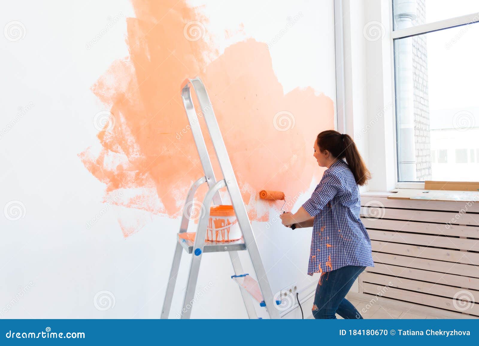 Mujer con un rodillo de pintura y pintura de pared naranja