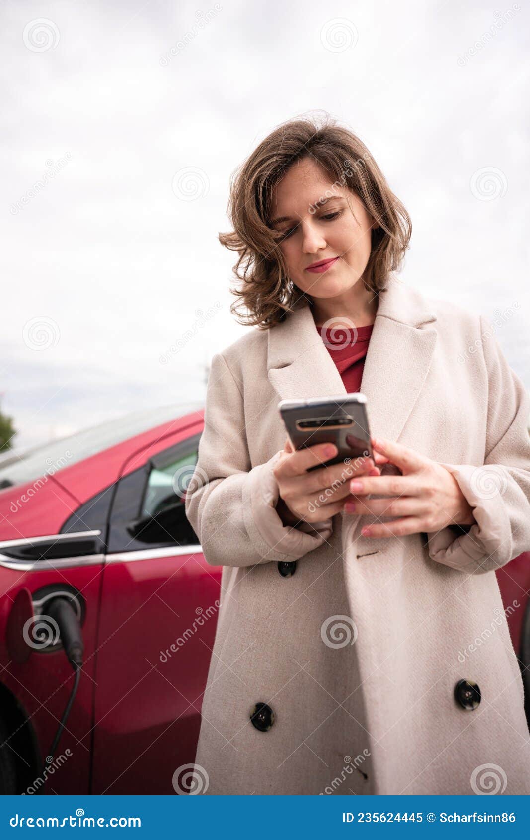 Mujer Con Abrigo Beige Con Smartphone Al Auto Eléctrico Imagen de archivo - Imagen de ocasional, rojo: 235624445