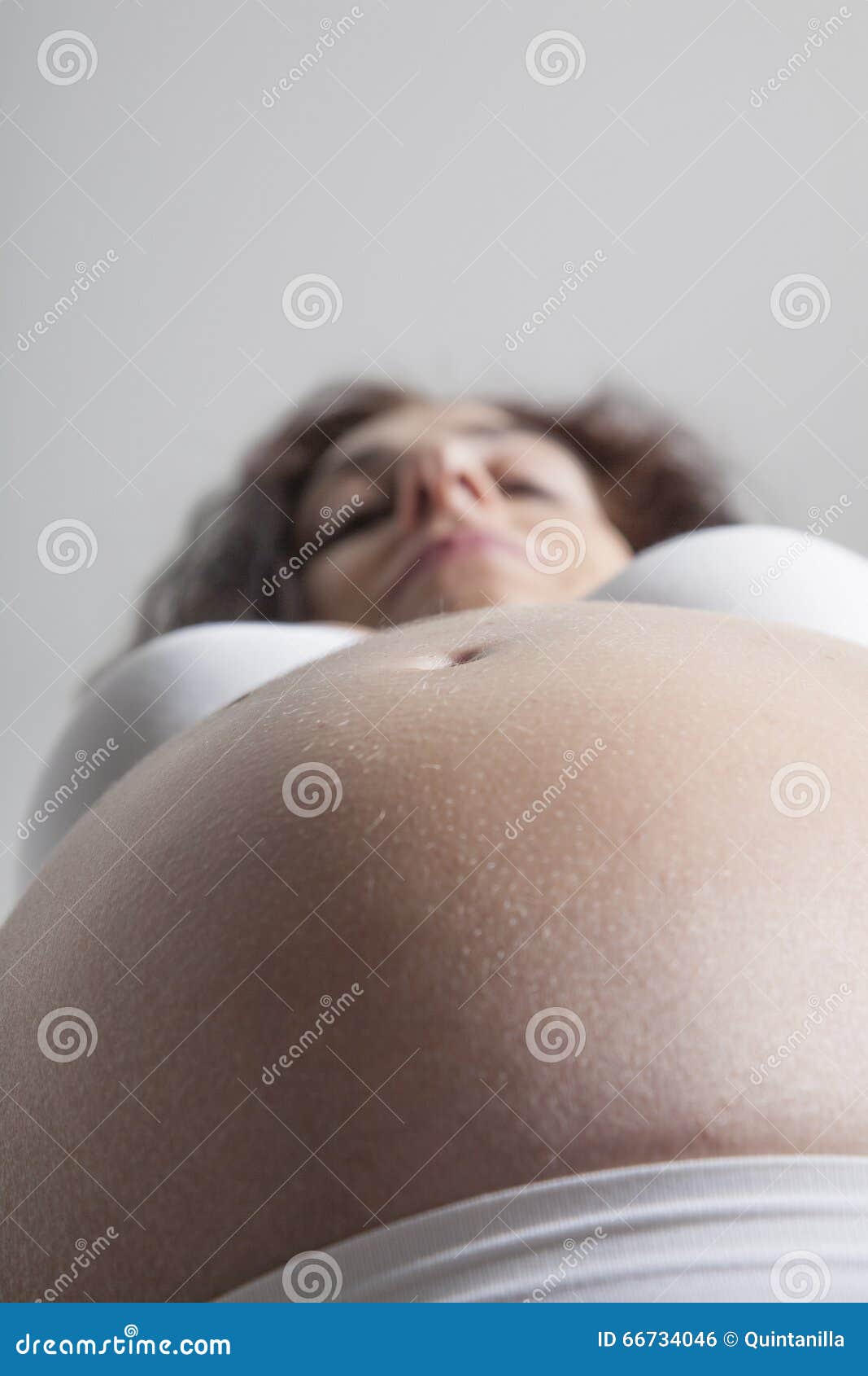 Ombligo del vientre desnudo de la mujer embarazada con el sujetador blanco.