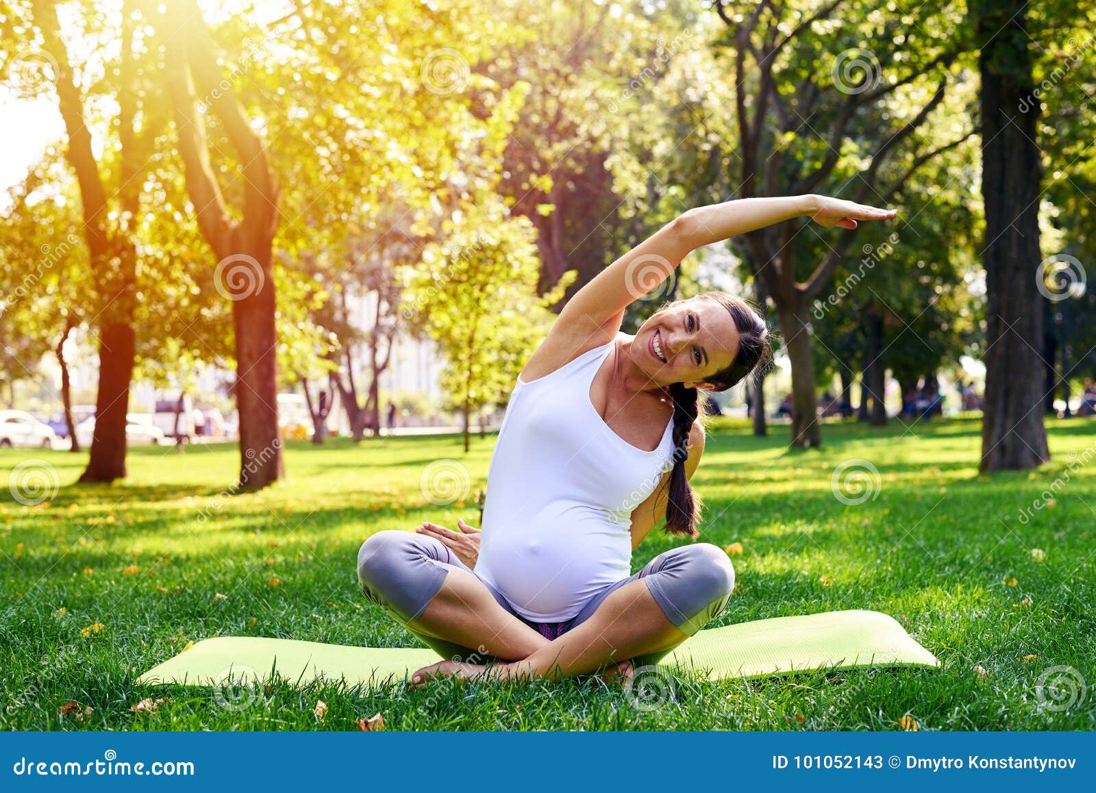 Primer de la mujer embarazada en la buena forma que estira en la estera de la yoga al aire libre