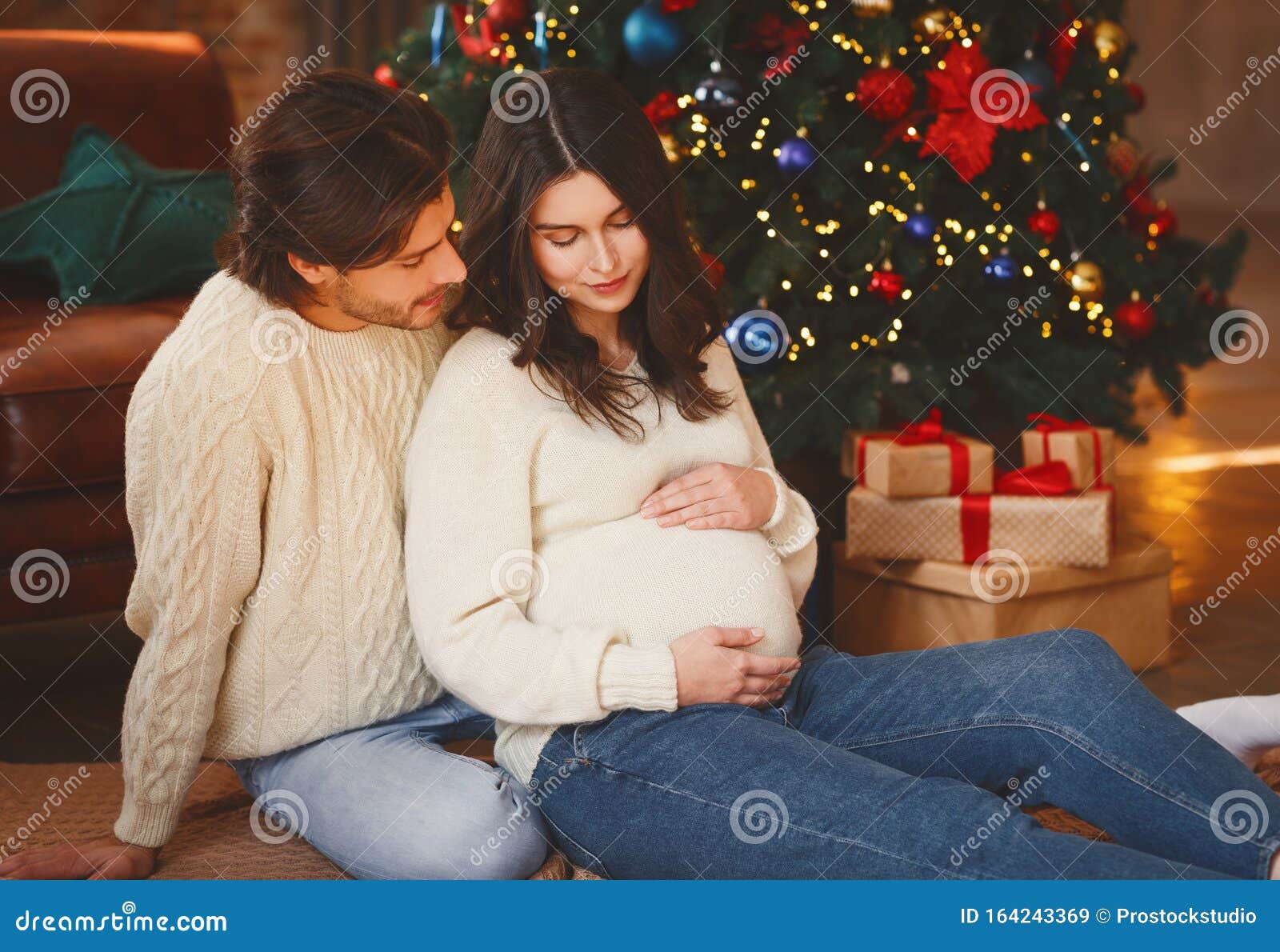 Mujer Embarazada Sentada Junto a Un árbol De Navidad Con Su Esposo Imagen de  archivo - Imagen de vacaciones, casero: 164243369