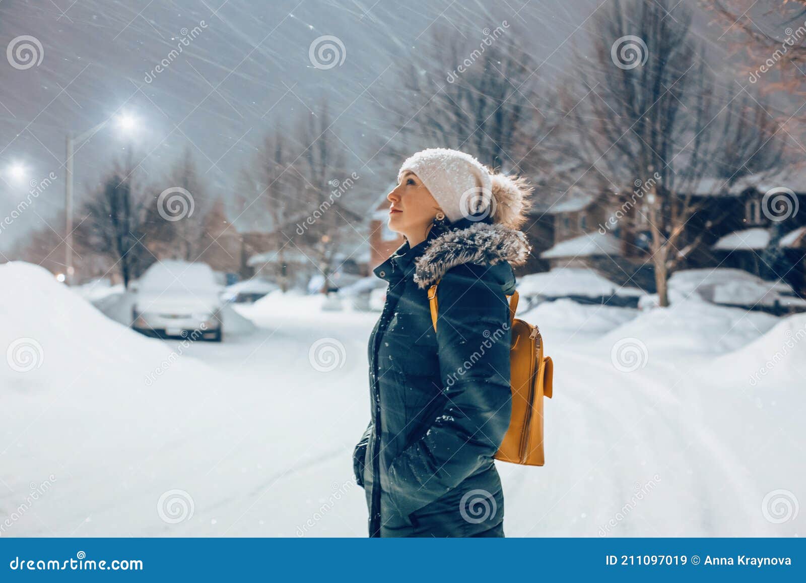 Mujer En Chaqueta Azul Ropa De Invierno Y Sombrero Caminando Al Aire Libre  Bajo La Nieve. Mujer De Pie Bajo La Luz De La Calle Mir Imagen de archivo -  Imagen de