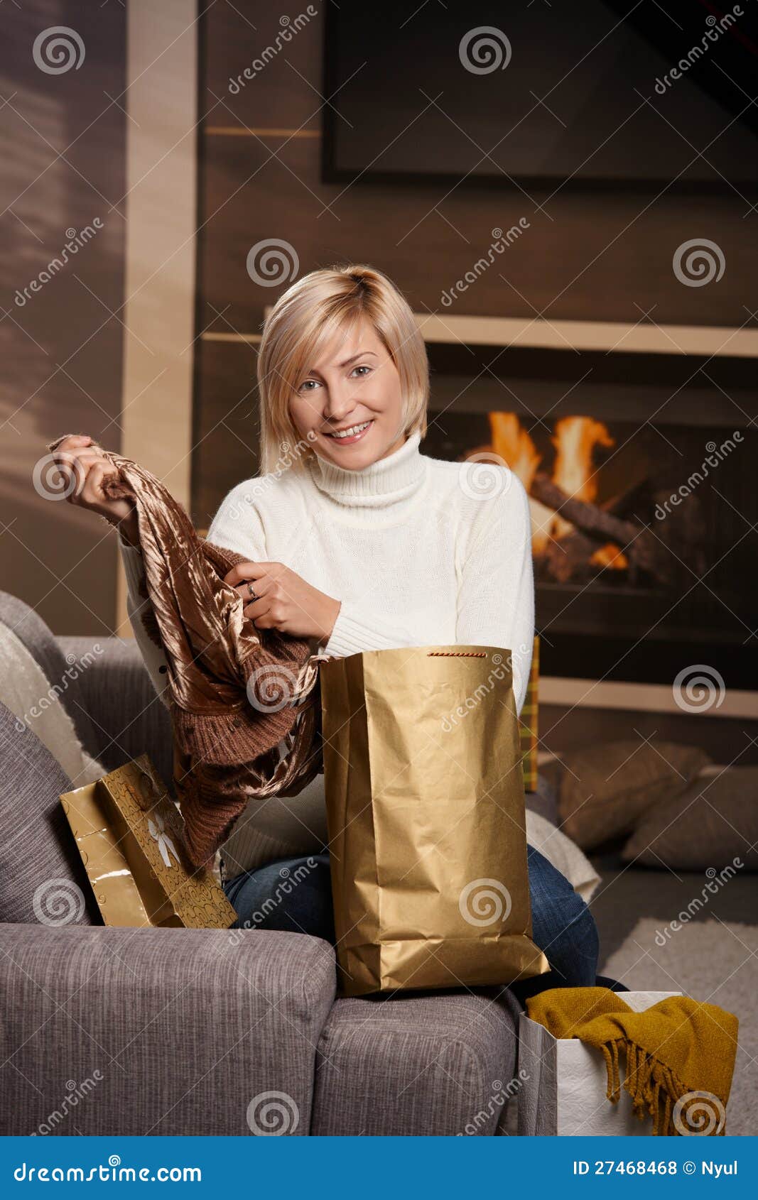 Mujer en el país con los bolsos de compras. La mujer joven feliz siiting en el sofá en el país que saca arropa de bolsos de compras. sonrisa.