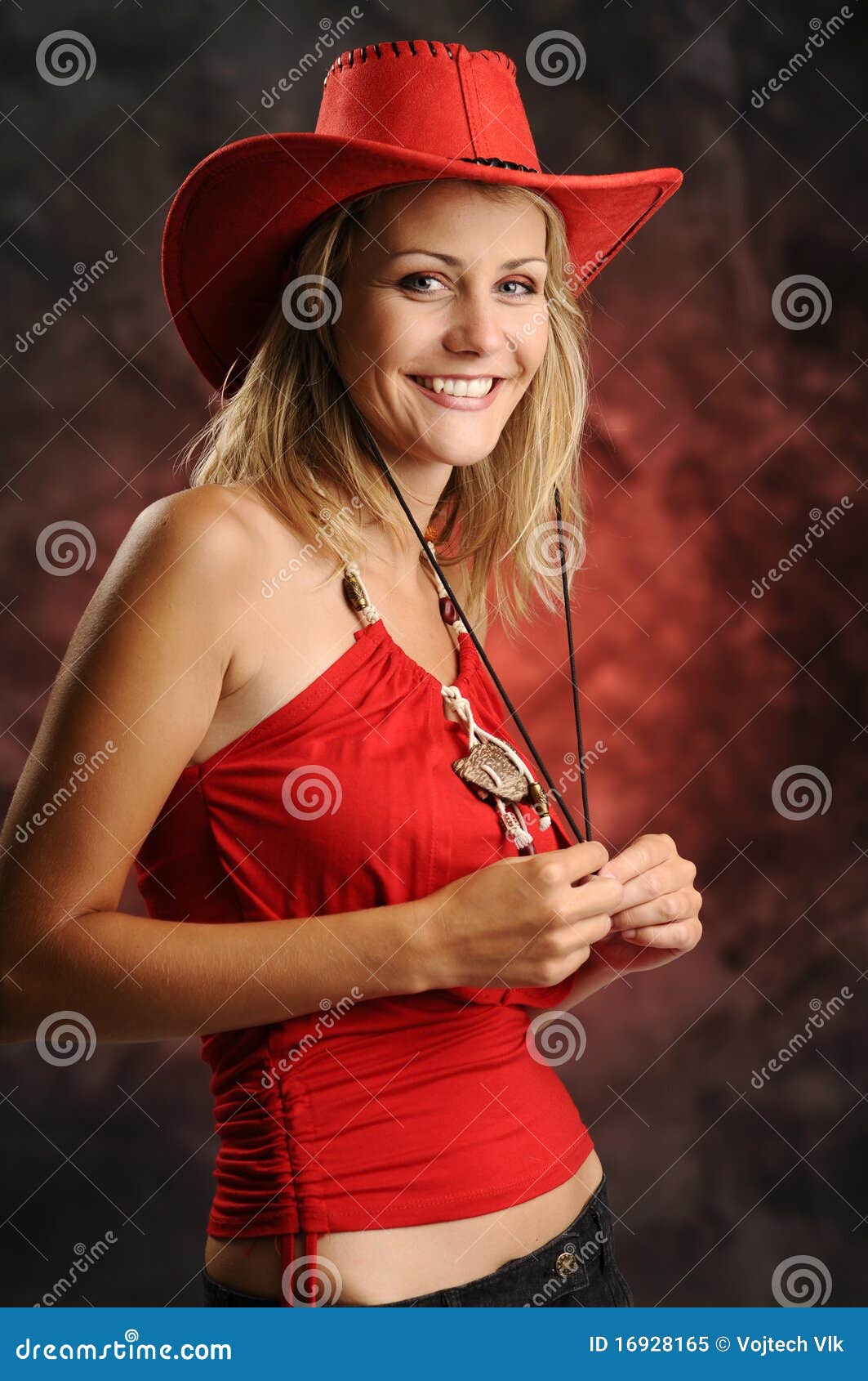 Mujer en rojo. La mujer rubia joven hermosa en camiseta roja y con el sombrero de vaquero rojo en fondo oscuro
