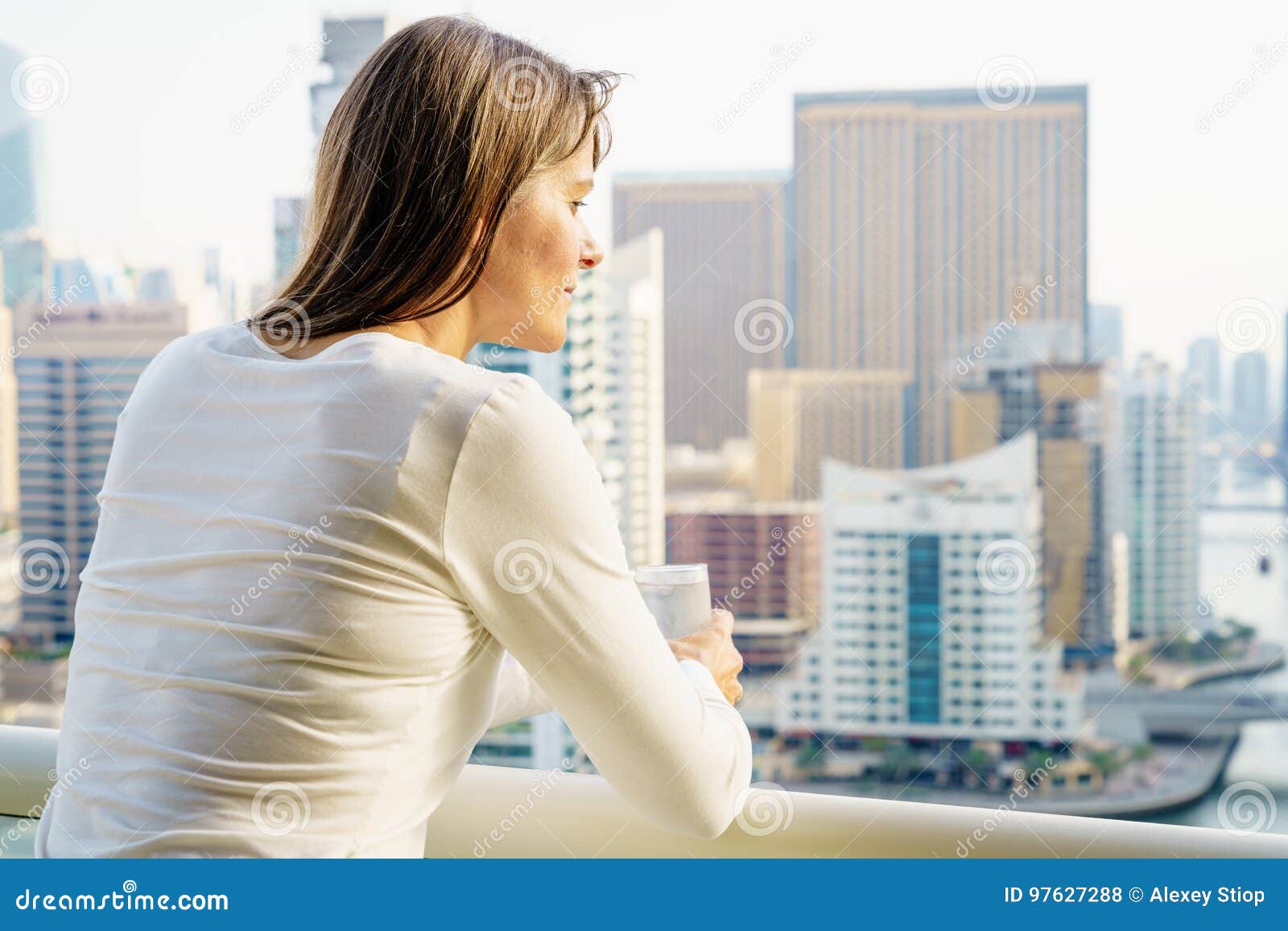 Mujer en un balcón del highrise. La mujer madura está disfrutando de la opinión de la ciudad de su balcón en el edificio de highrise