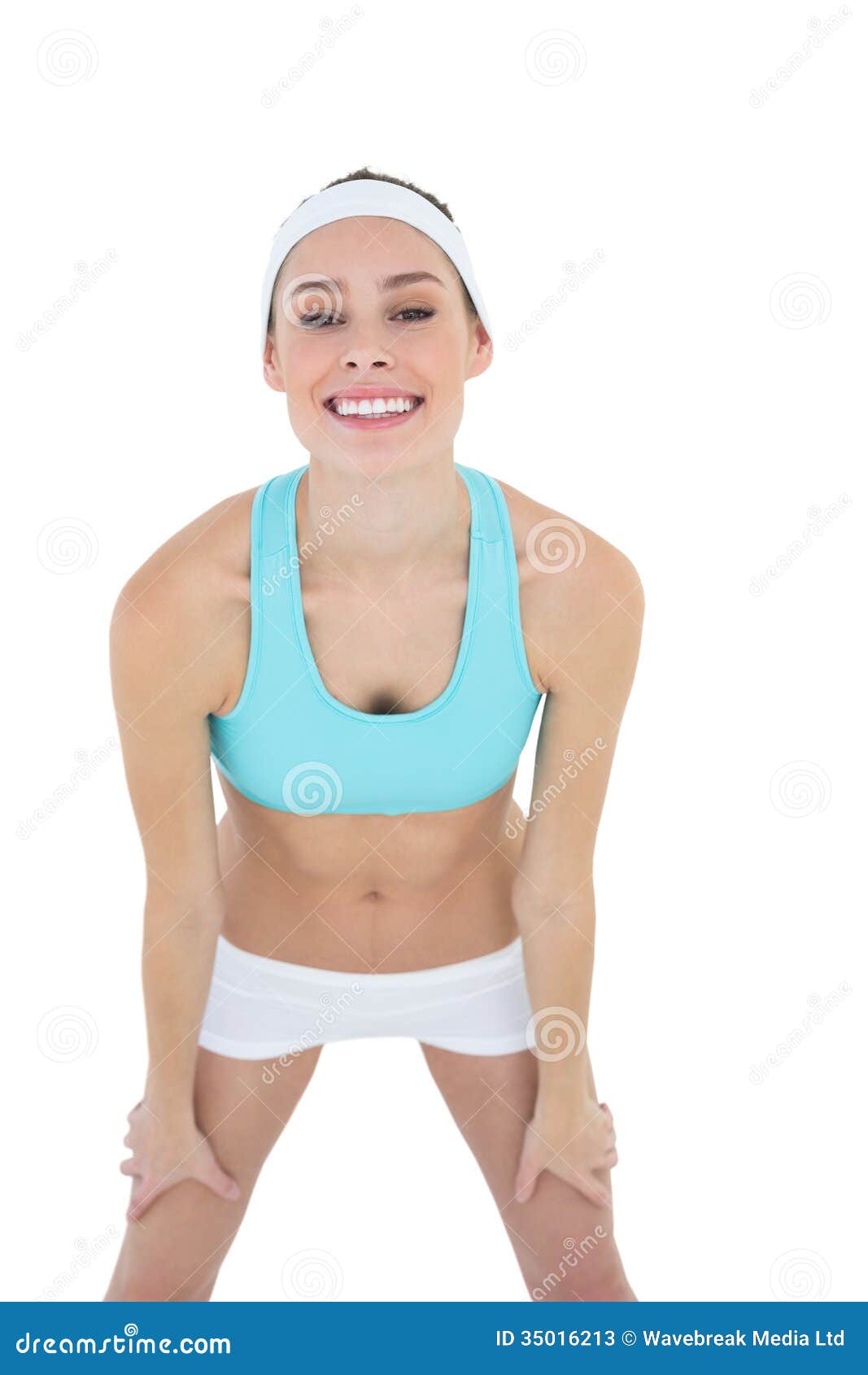 Mujer feliz hermosa que presenta la ropa de deportes que lleva que mira alegre la cámara en la pantalla blanca