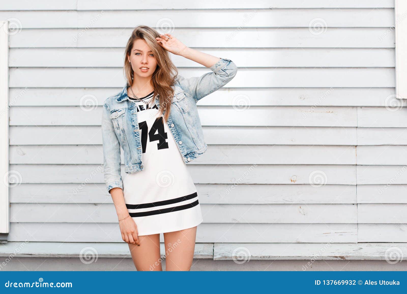 Mujer Joven Elegante Americana En Una Chaqueta Azul Del Dril Algodón Del Verano En Un Vestido Blanco Deportivo En Actitudes Ne Foto de archivo - Imagen de vaqueros, manera: 137669932