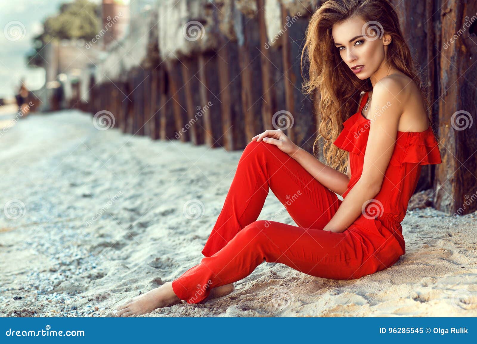 Joven Encantadora Con El Pelo En El Mono Coralino Del Hombro Del Rojo Uno Que Se Sienta En La Playa En Las Pilas Oxid Imagen de archivo Imagen de