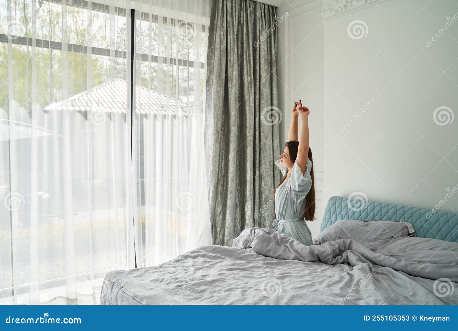 Mujer Joven Parada Y Abriendo Cortinas Blancas En La Ventana La Mañana  Después De Despertarse En El Dormitorio De Su Casa Imagen de archivo -  Imagen de adulto, despierto: 255105353