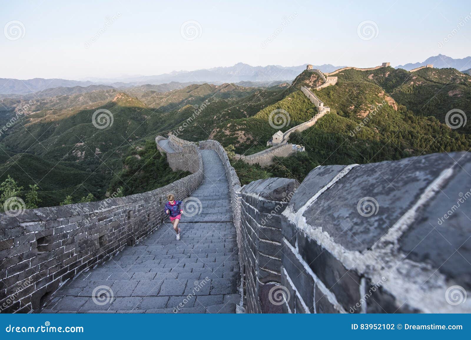 Mujer joven que corre en la Gran Muralla china en verano en salida del sol