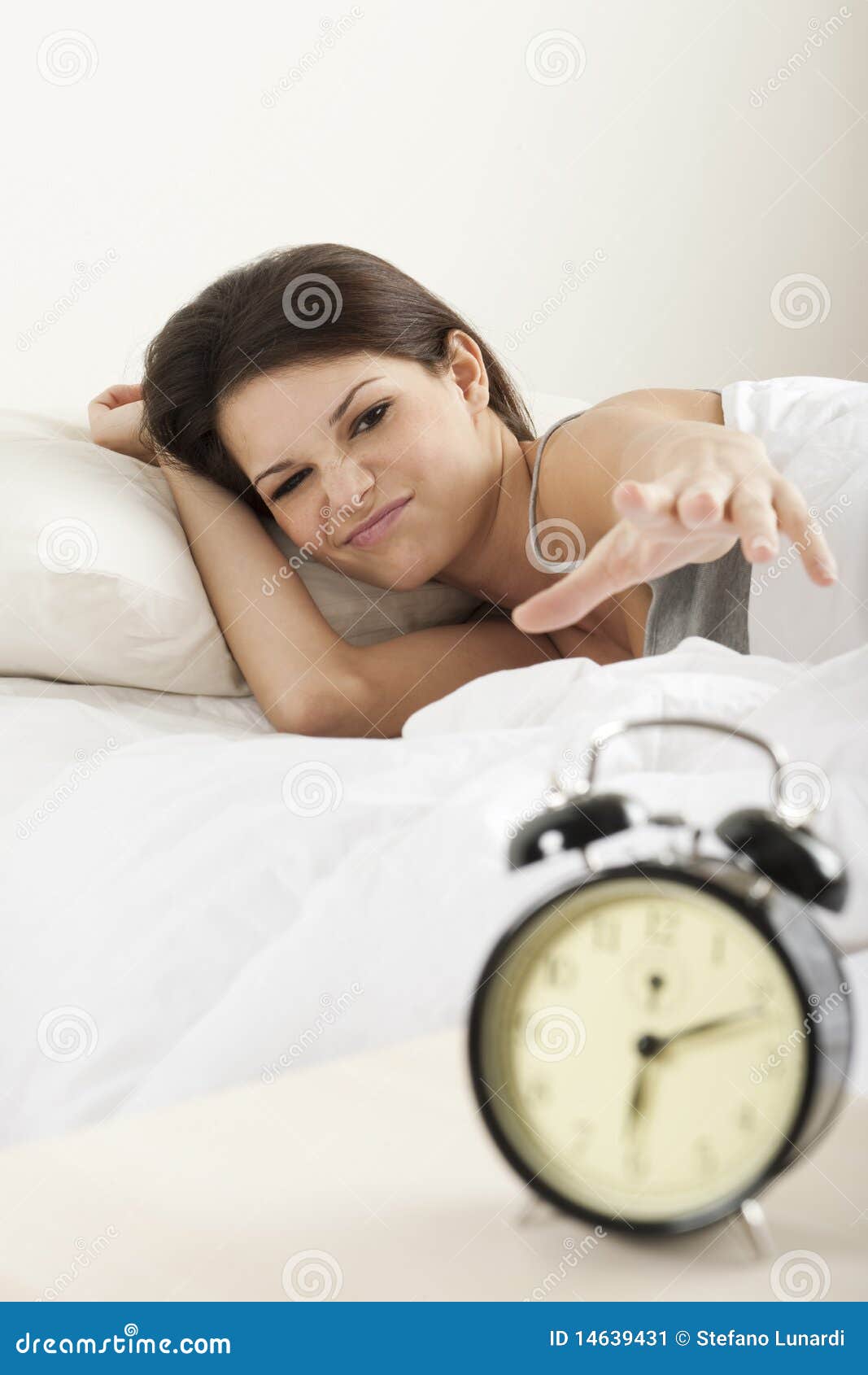 Mujer joven que despierta por la mañana, intentando suspender un reloj de alarma