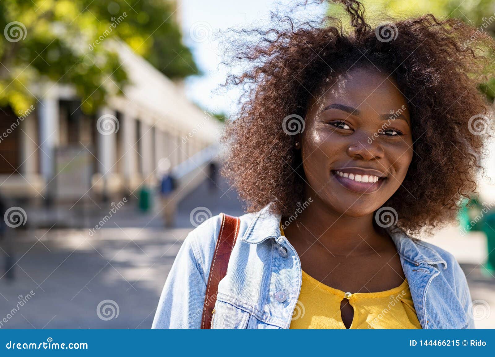 Mujer negra feliz con curvas. Retrato de la mujer afroamericana joven con el pelo rizado que sonríe y que mira la cámara Muchacha con curvas negra en el goce de la ropa casual al aire libre Estudiante universitario negro bonito en campus