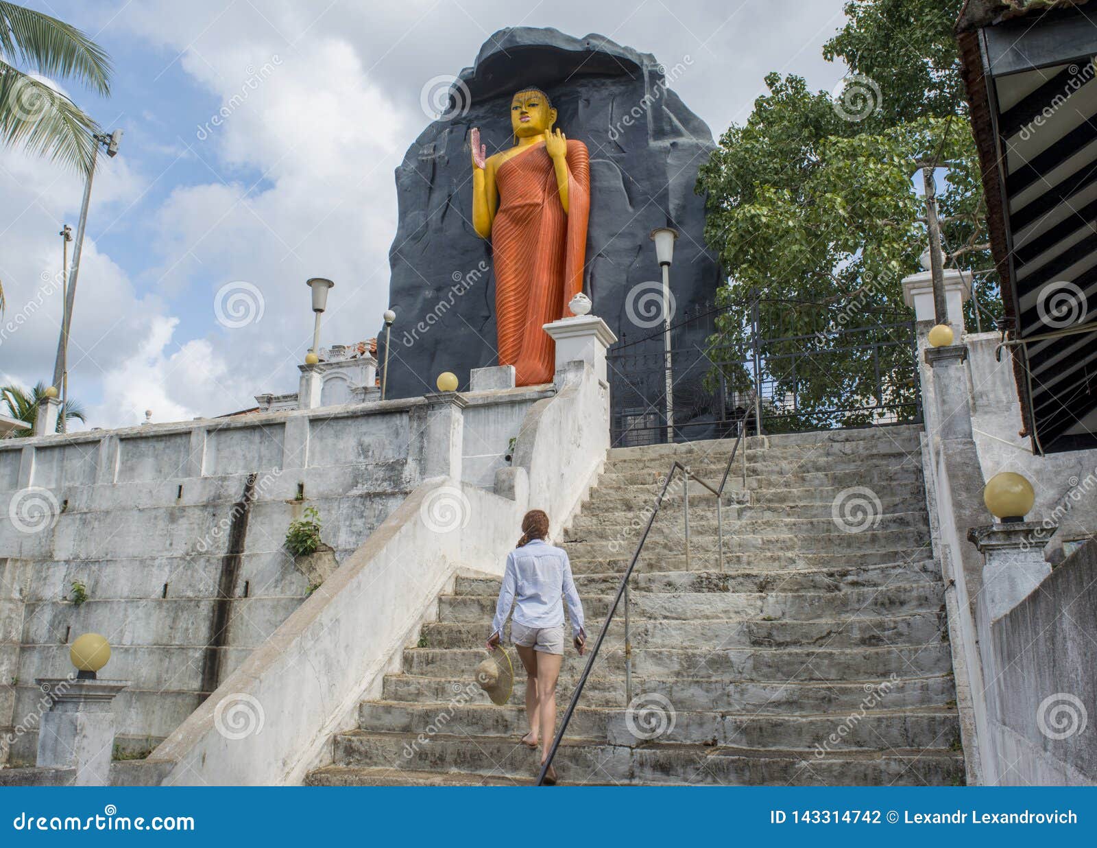 Mujer que camina hacia la estatua antigua enorme de Buda en la yarda del templo en Sri Lanka