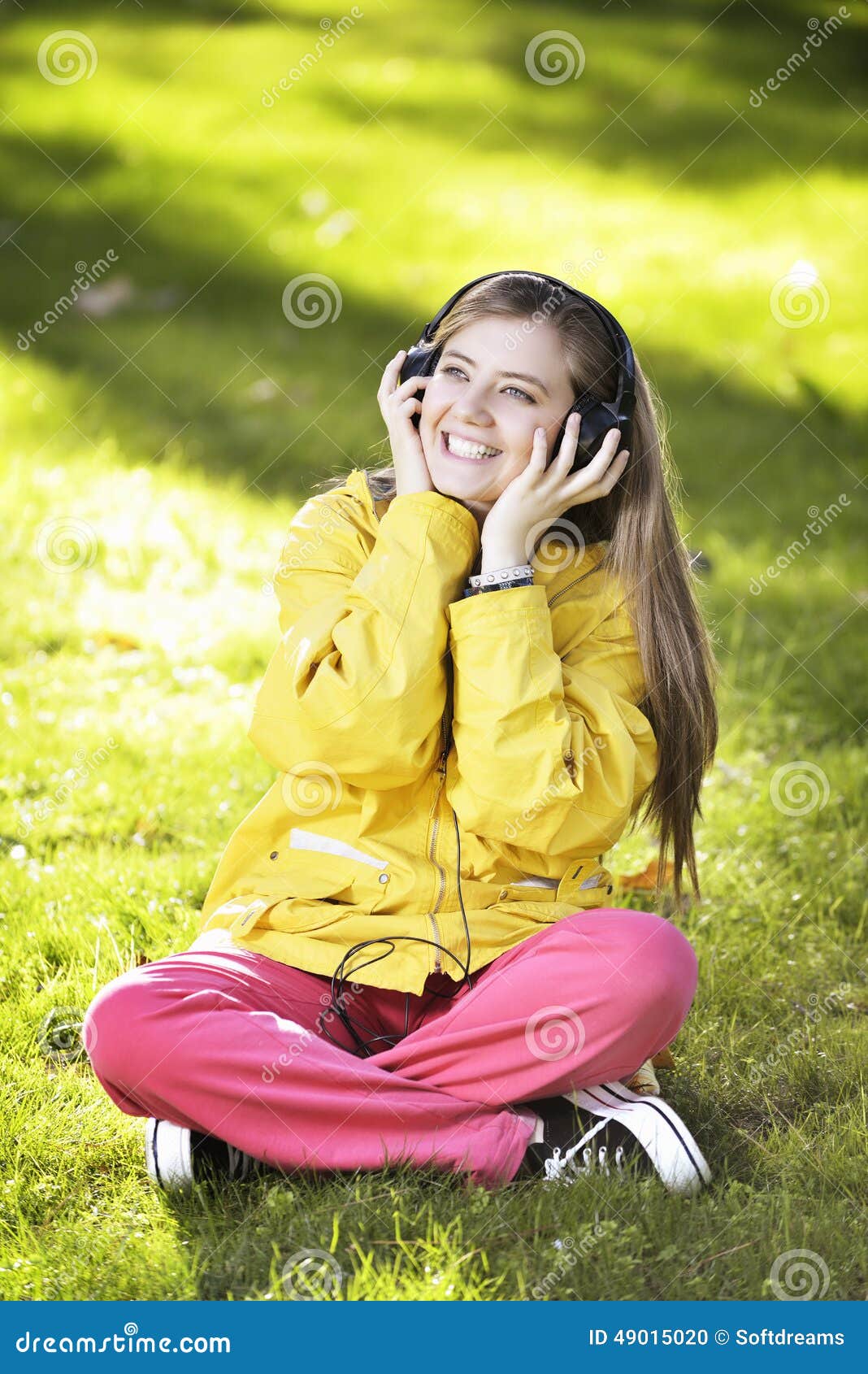 Mujer que escucha la música Muchacha del estudiante femenino afuera en el parque que escucha la música en los auriculares mientras que estudia Estudiante universitario joven feliz de la pertenencia étnica asiática y caucásica mezclada