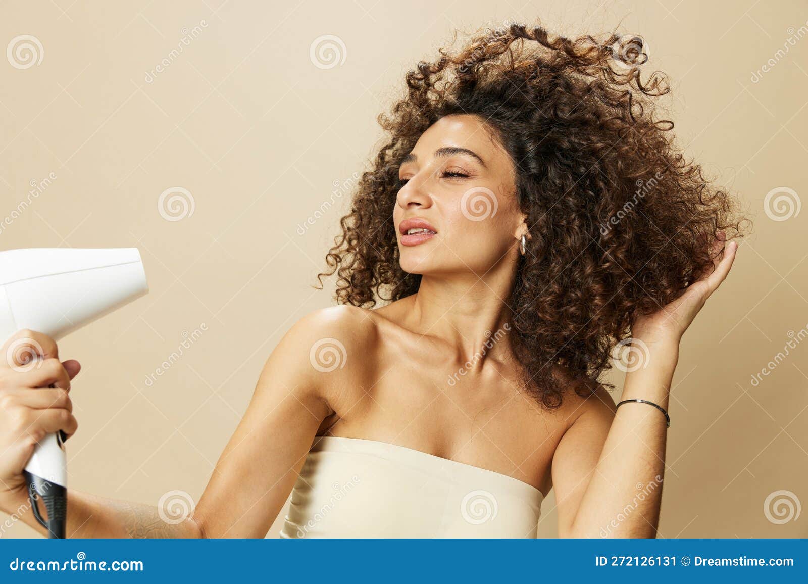 Mujer joven feliz con secador de pelo después de su cabello rizado en un  baño.