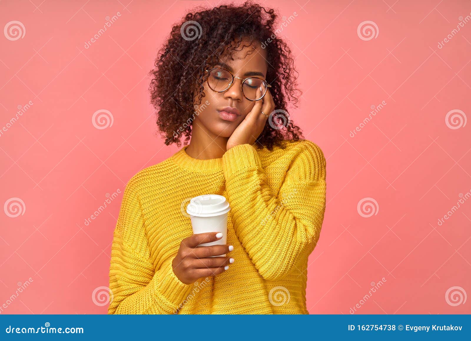 Só o café pode me refrescar. mulher afro-americana sonolenta e cansada  cobre metade do rosto com a palma da mão, tem expressão triste, fecha os  olhos, carrega um copo descartável de bebida com cafeína, continua  trabalhando.