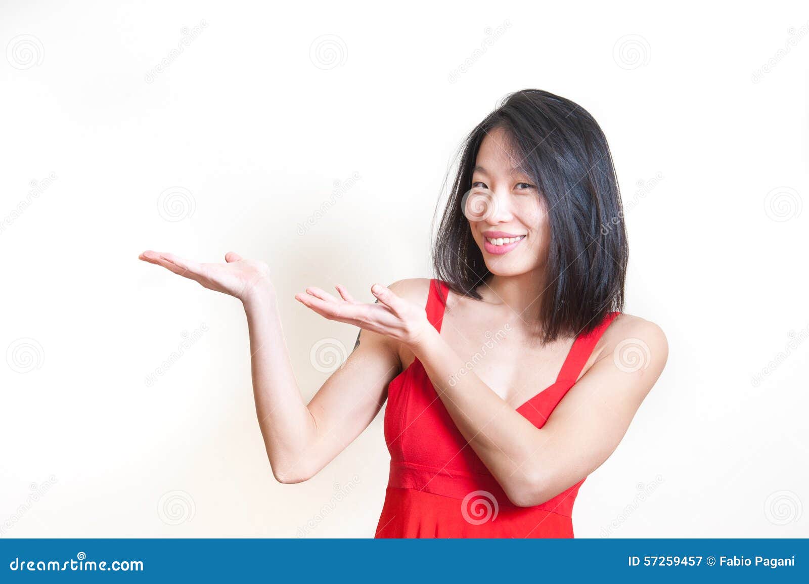 Mulher asiática bonita nova no vestido vermelho no fundo branco. Young beautiful asian woman in red dress smiling and pointing out on white background