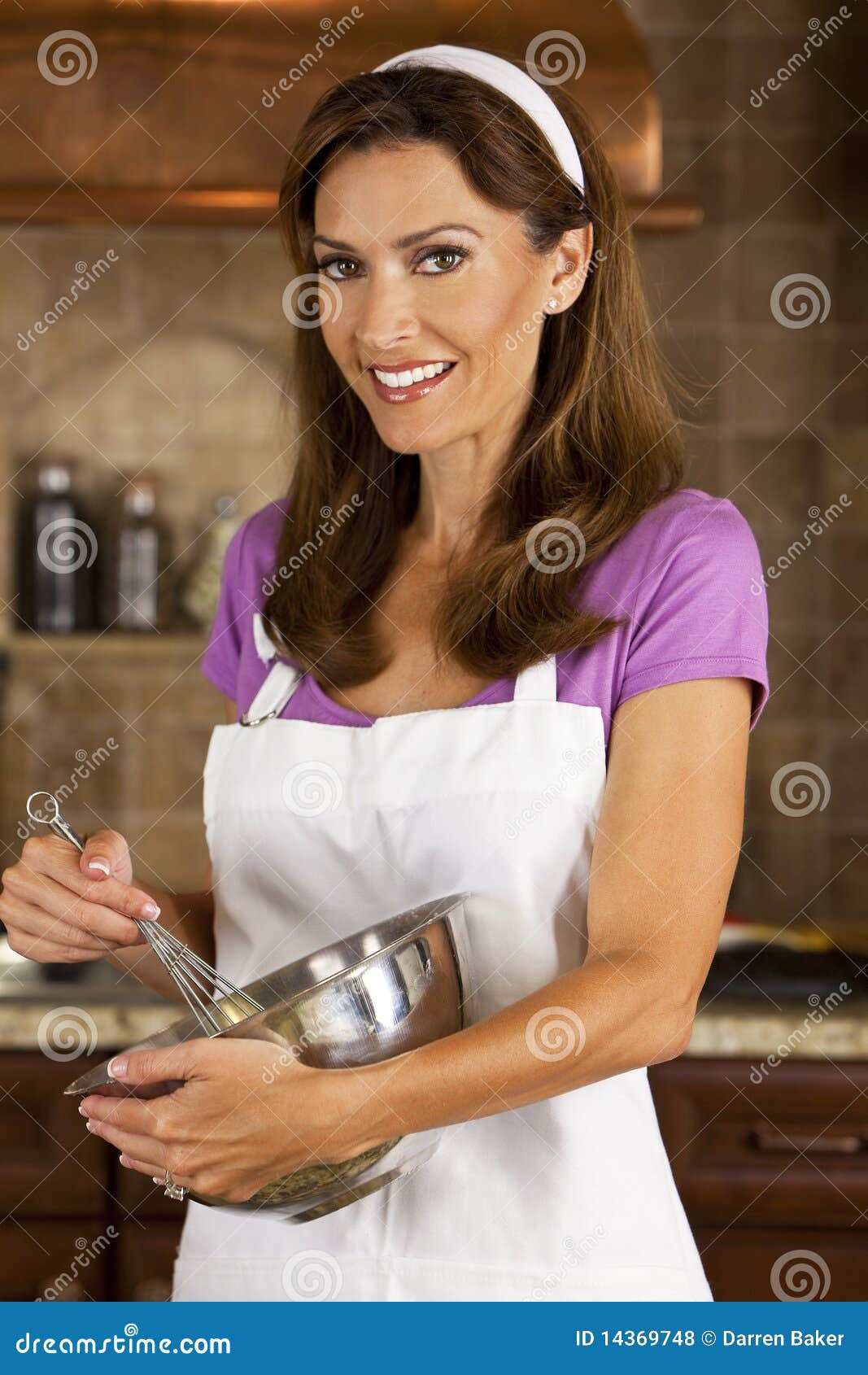 Mulher atrativa que mistura &amp; que coze na cozinha. Uma mulher de sorriso atrativa, uma mamã americana típica, misturando e cozendo em sua cozinha