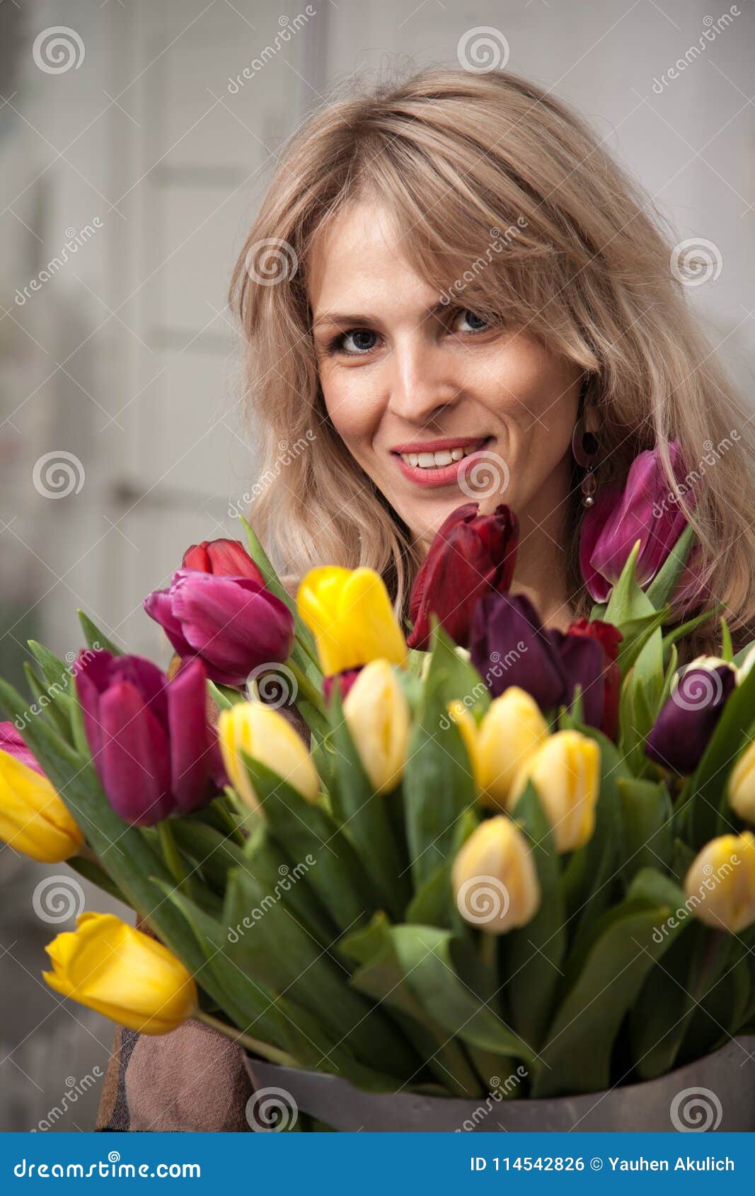 A mulher bonita com um ramalhete das tulipas floresce em uma cubeta do metal. A menina bonita com tulipas floresce nas mãos em um fundo claro