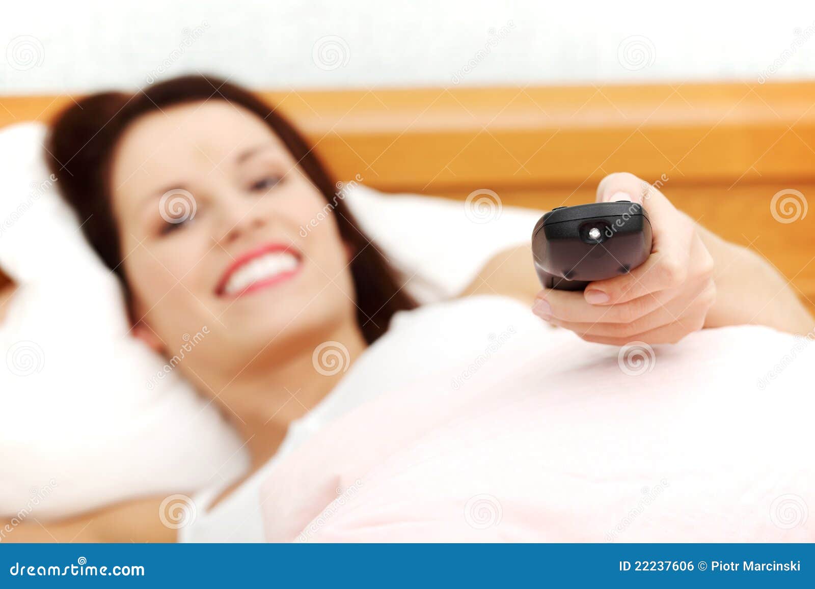 Mulher bonita na cama que prende um de controle remoto. Close up da vista dianteira dos canais de televisão em mudança de sorriso novos bonitos de uma mulher com o de controle remoto.