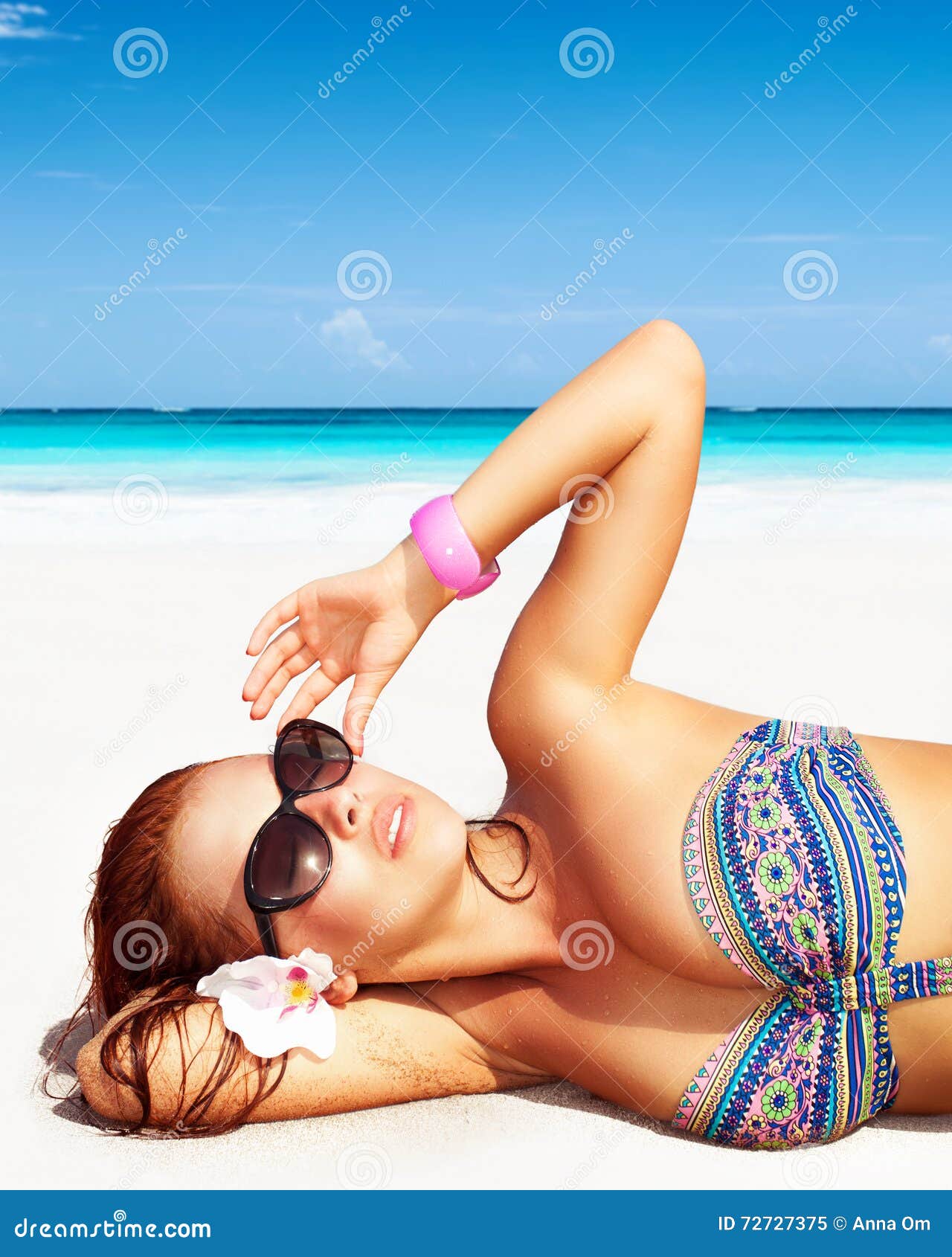Retrato de uma mulher bonita na praia, óculos de sol vestindo, encontrando-se para baixo na costa arenosa branca limpa, apreciando termas do dia em um recurso tropical, férias de verão luxuosas