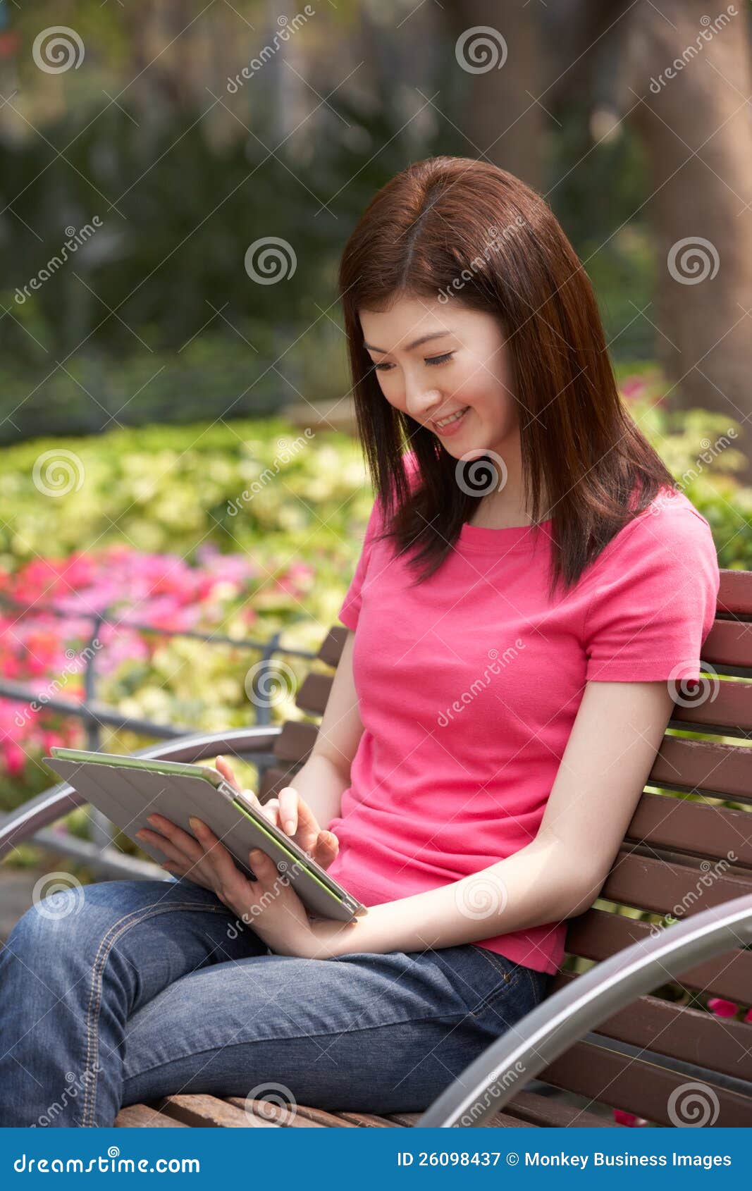 Mulher chinesa nova que usa a tabuleta de Digitas enquanto relaxando no banco de parque