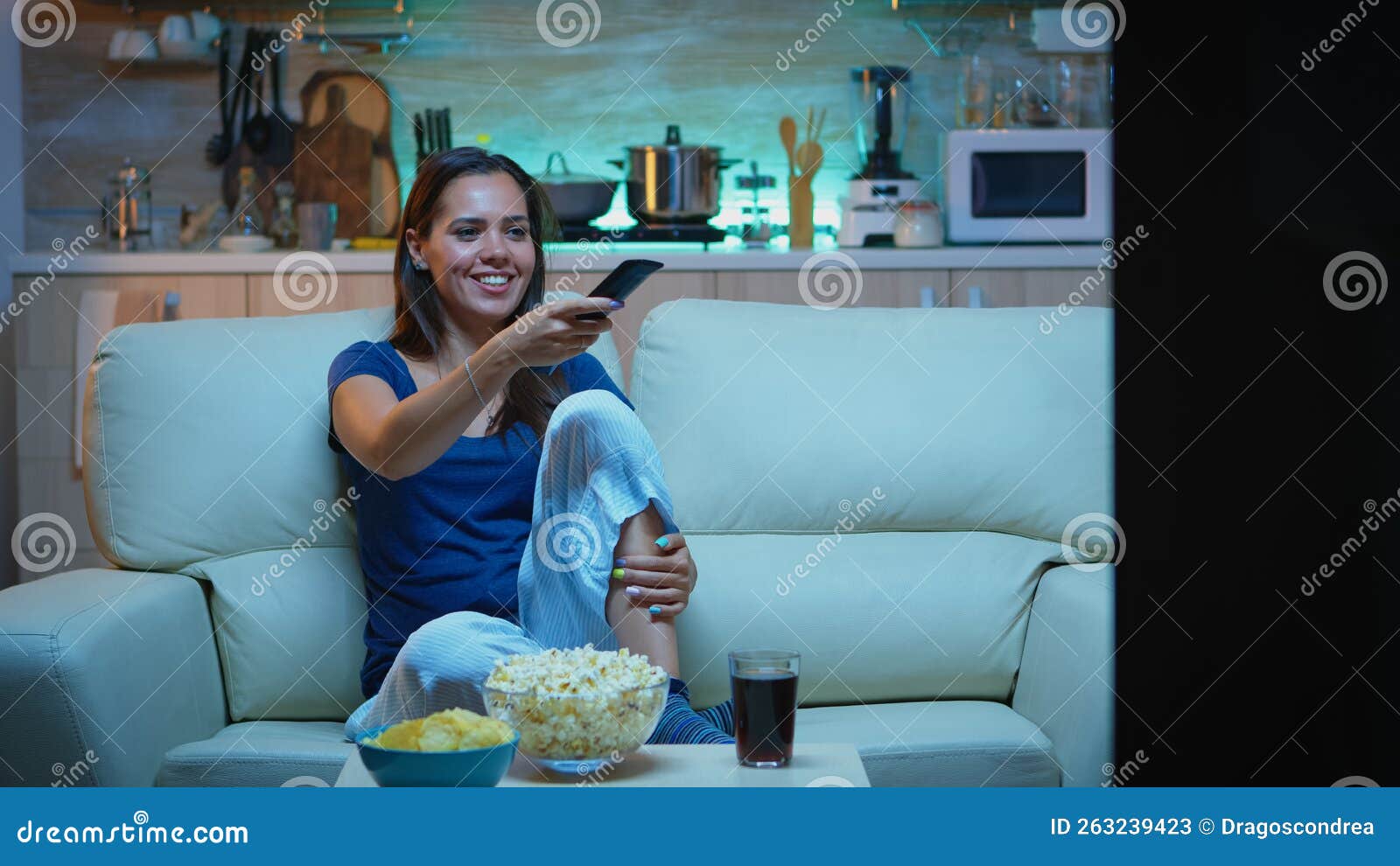 Mulher jovem comendo batata frita assistindo filme na mesa azul