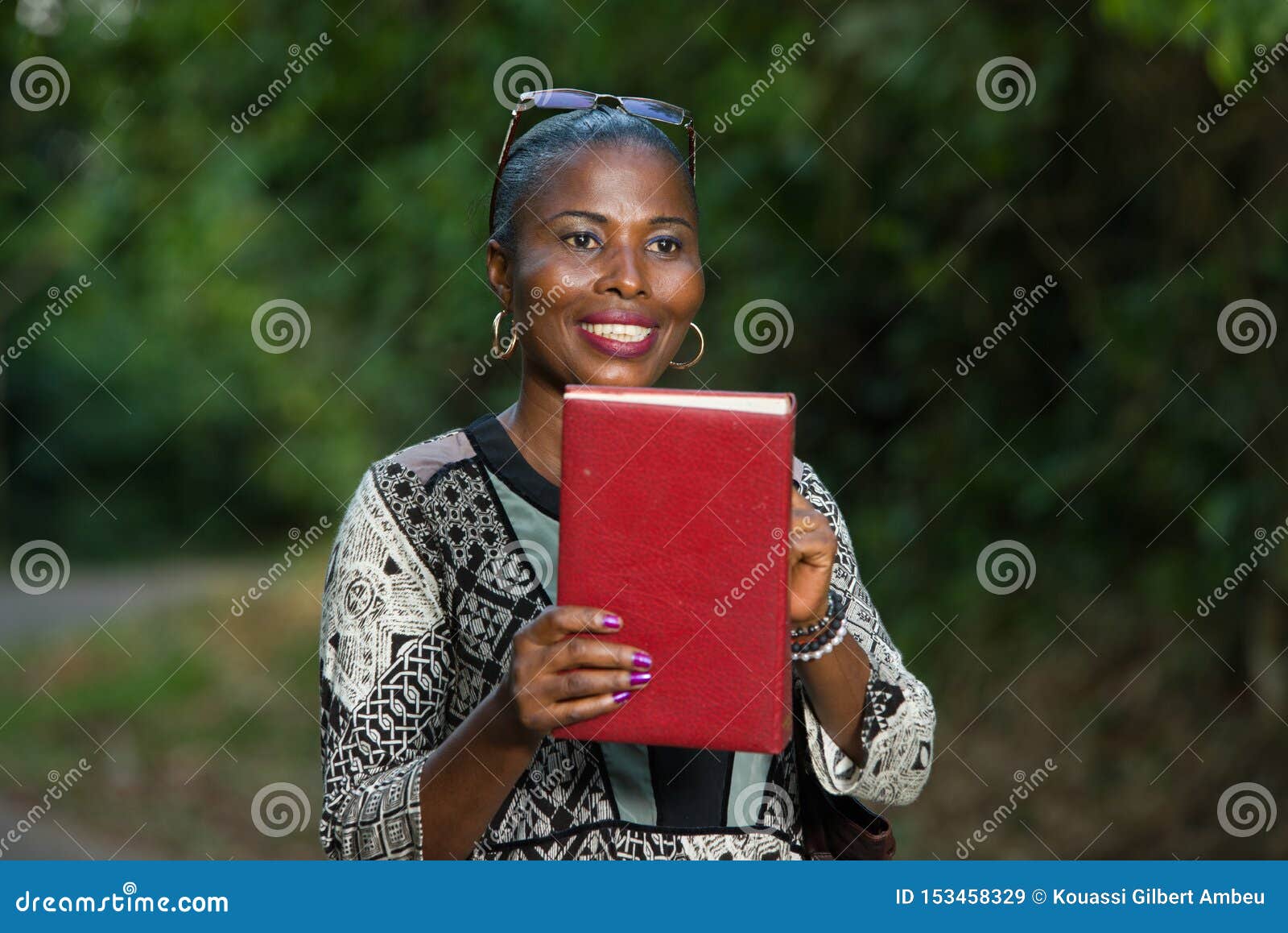 Mulher de sorriso apenas na natureza que guarda um livro. Mulher de sorriso apenas na natureza que realiza e que mostra um livro vermelho na floresta após um dia do passeio e da leitura Leitura e férias do conceito