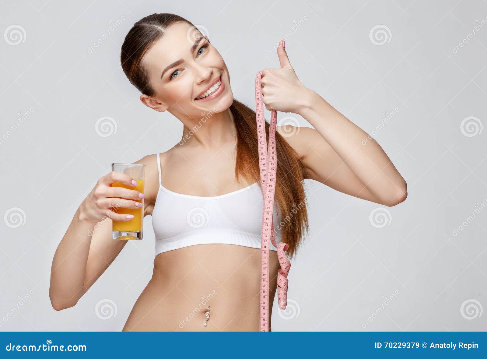 Mulher desportiva sobre o fundo cinzento que guarda o vidro do suco de laranja