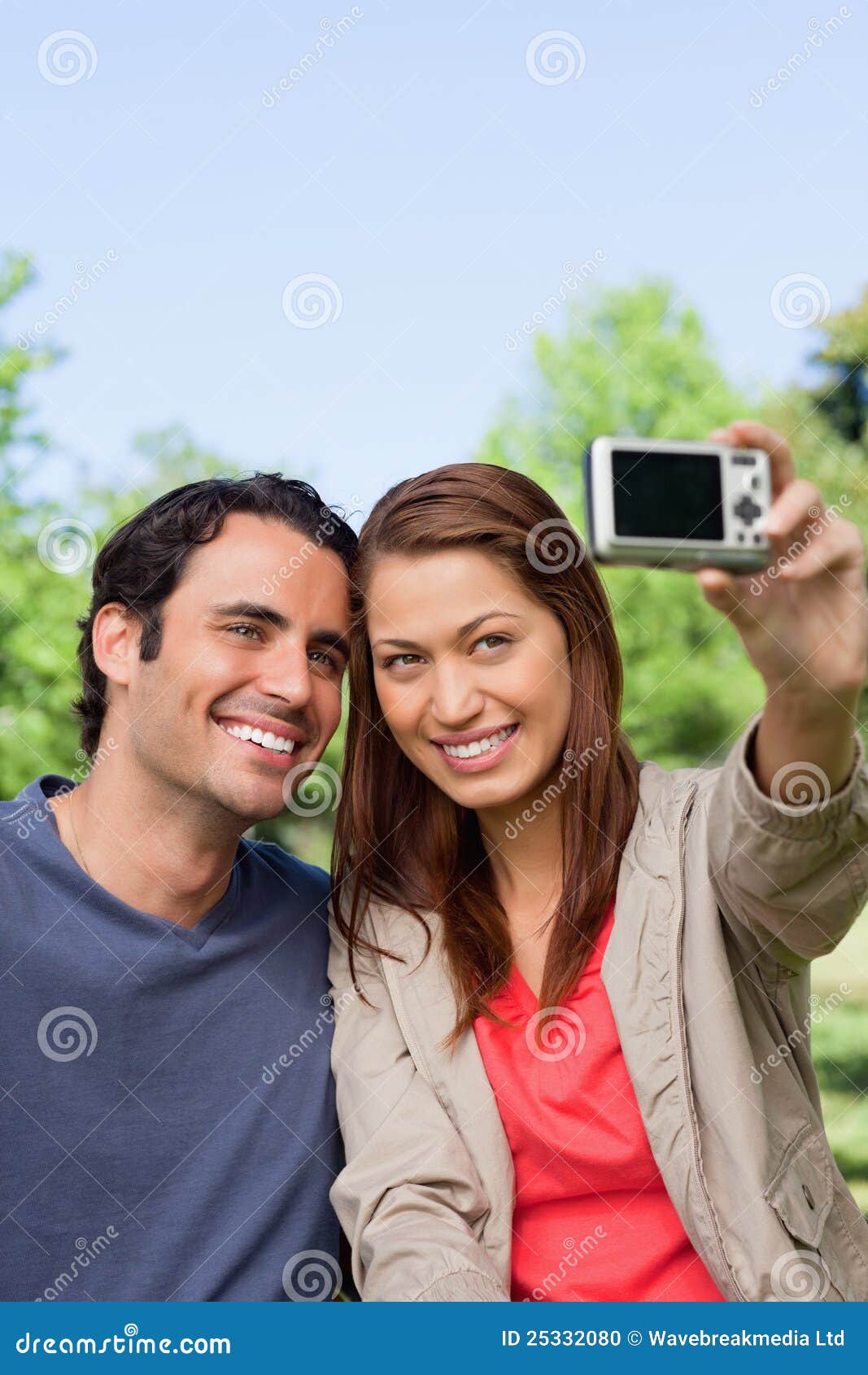 Mulher e seu amigo que olham para sua câmera para uma imagem de. A mulher guardara uma câmera nos braços alcança para tomar uma imagem de seu amigo e de ela mesma em um ambiente aberto da pastagem