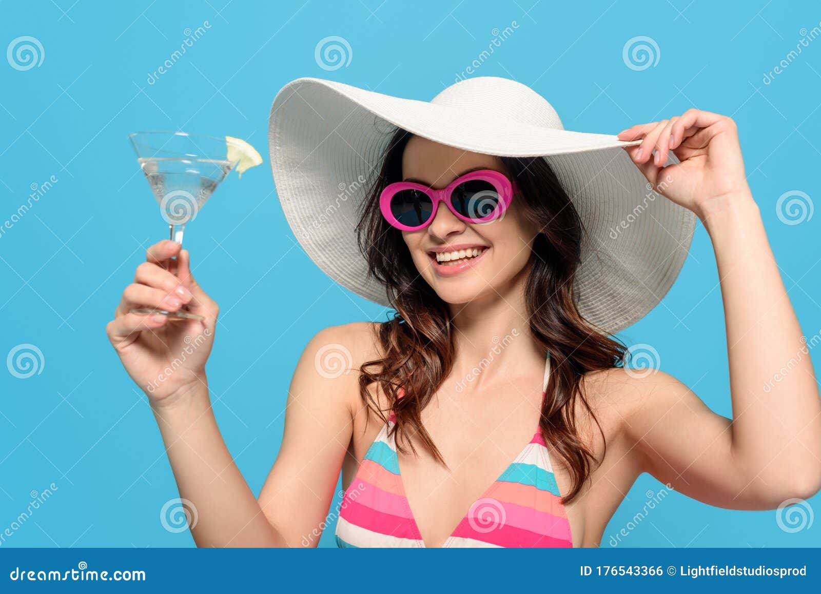 Uma mulher de chapéu e óculos de sol está sentada à mesa com um coquetel.