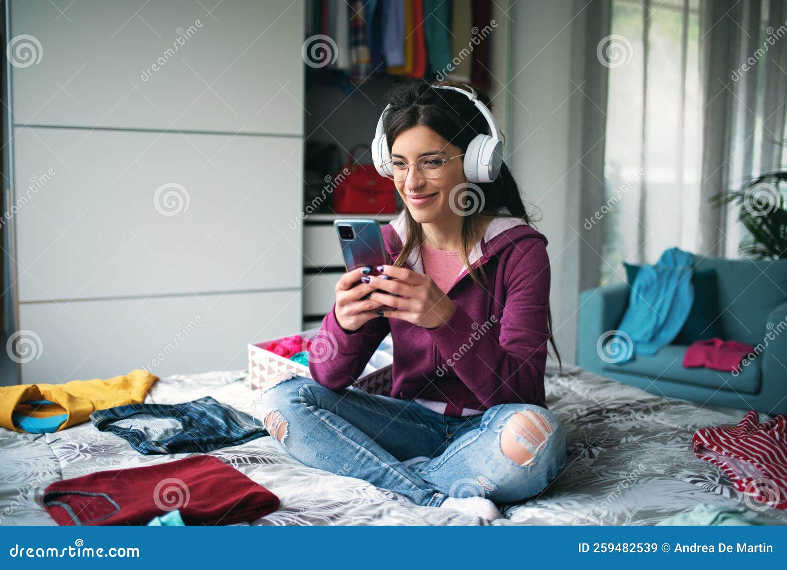 Mulher feliz relaxando no quarto e conversando. Jovem feliz relaxando em seu quarto ela está usando fones de ouvido e conversando com seu smartphone