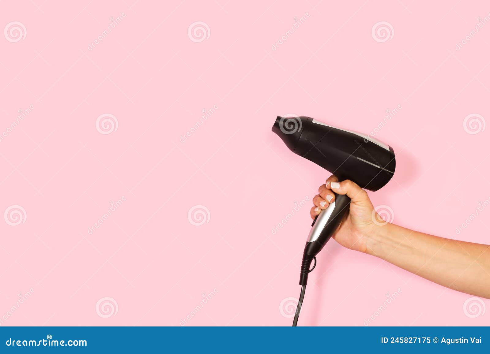 Secador de cabelo preto na mão de uma mulher em um fundo rosa