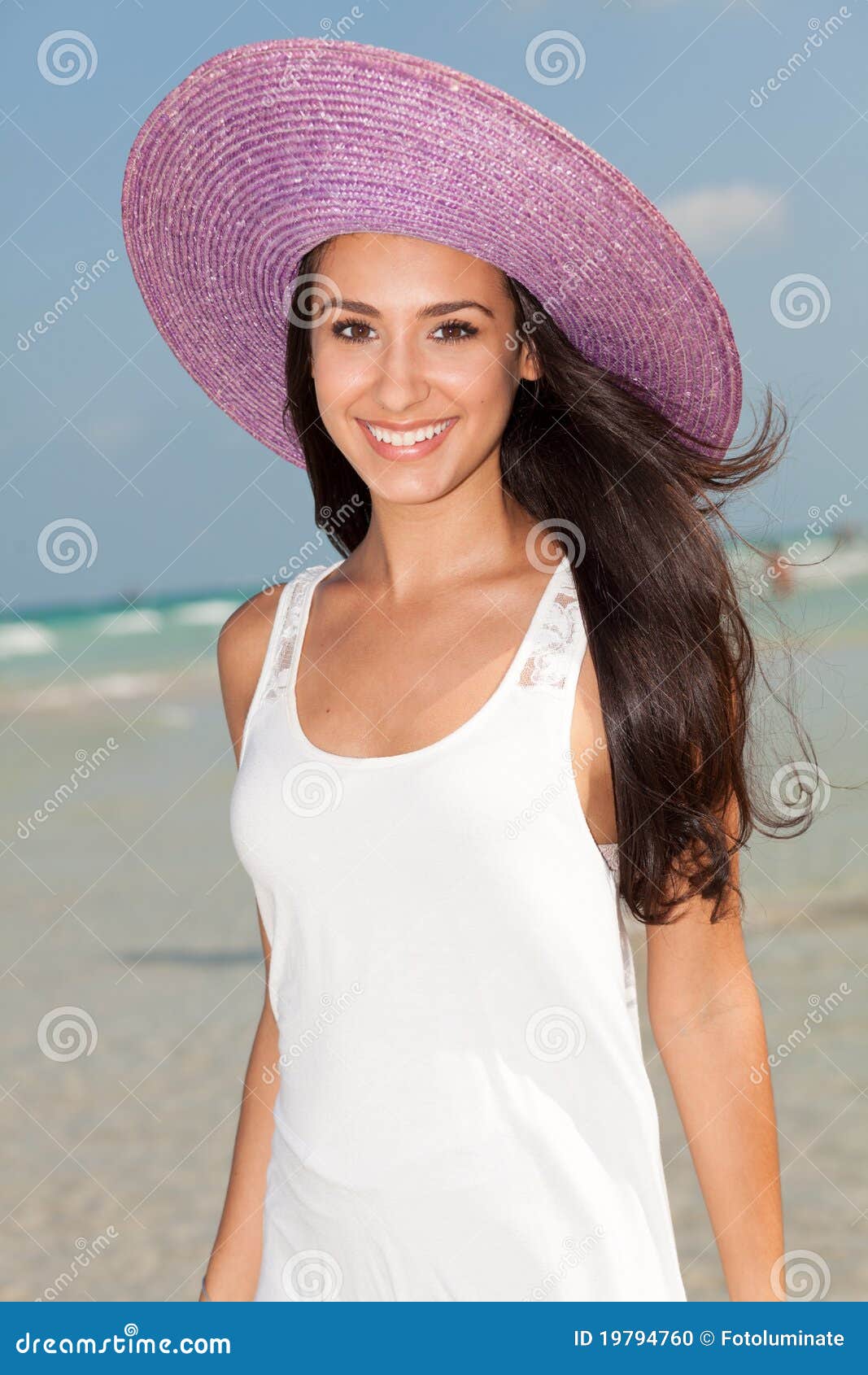 Mulher nova bonita em Miami Beach. Mulher nova bonita que desgasta um chapéu roxo extravagante que aprecia o cristal como novo - linha costeira desobstruída de praia sul bonita em Miami.