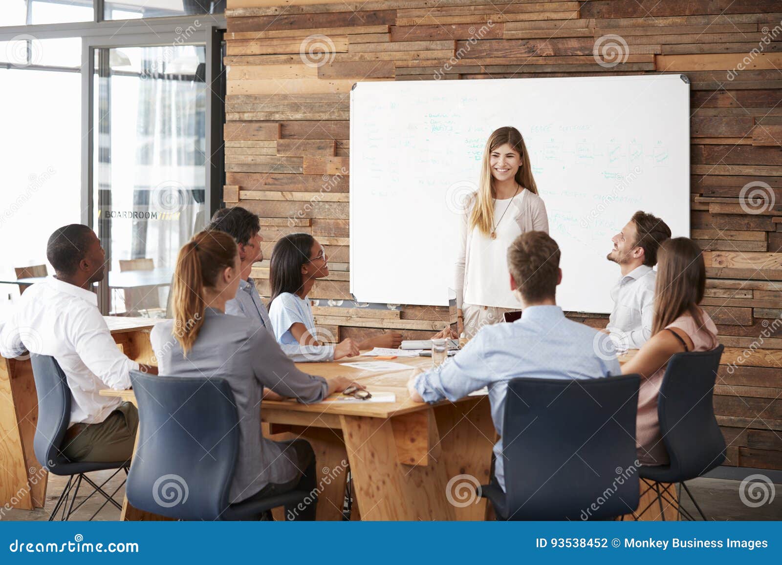 Mulher que dá uma apresentação no whiteboard à equipe do negócio. Mulher que dá uma apresentação no whiteboard à equipe do negócio