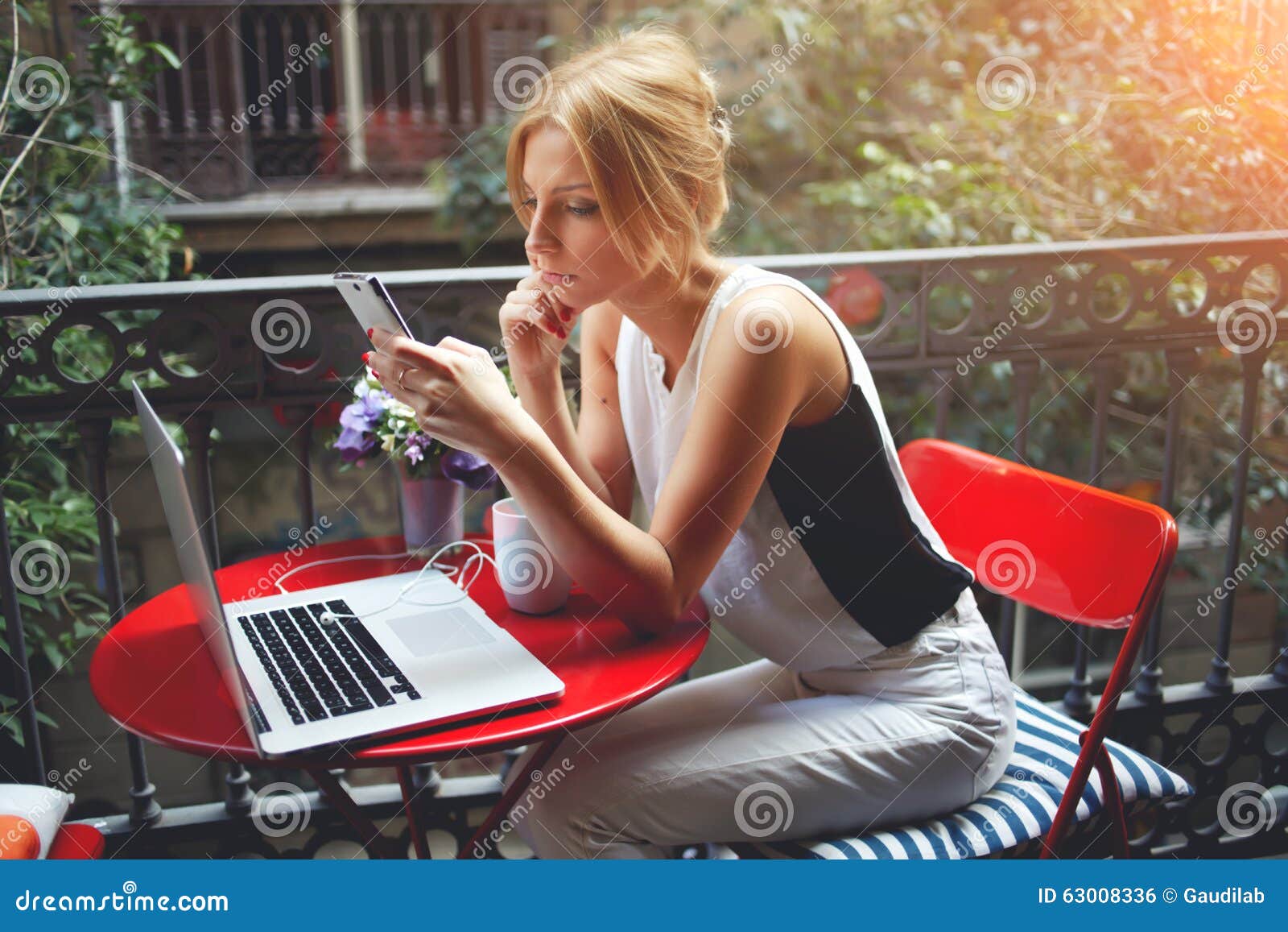 Mulheres bonitas que leem notícias em seu telefone de pilha ao relaxar após ter visto o filme no laptop portátil. Telefone celular de utilização fêmea novo após o trabalho no rede-livro durante o tempo da recreação