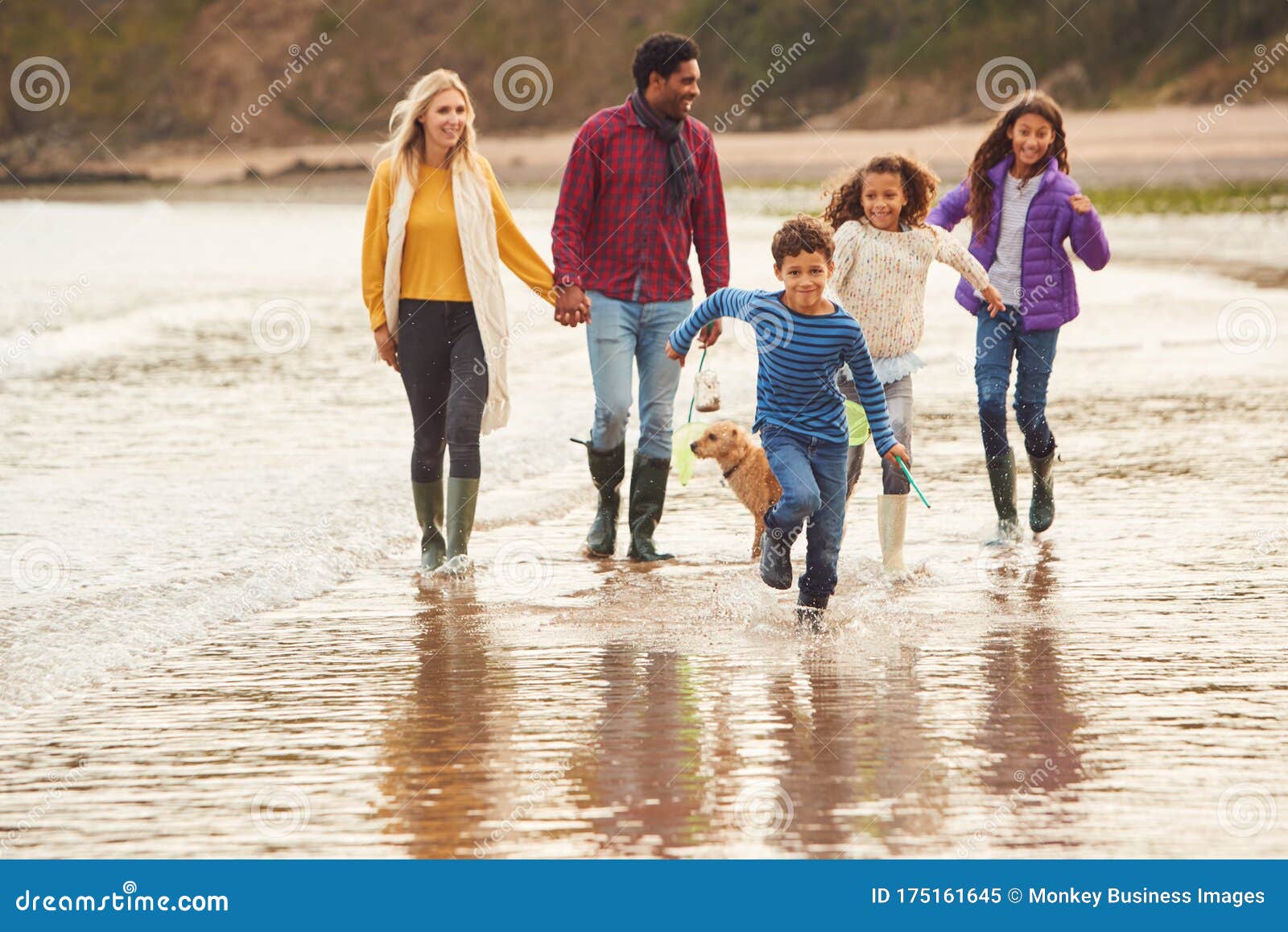multi-cultural family with pet dog walking along beach shoreline on winter vacation