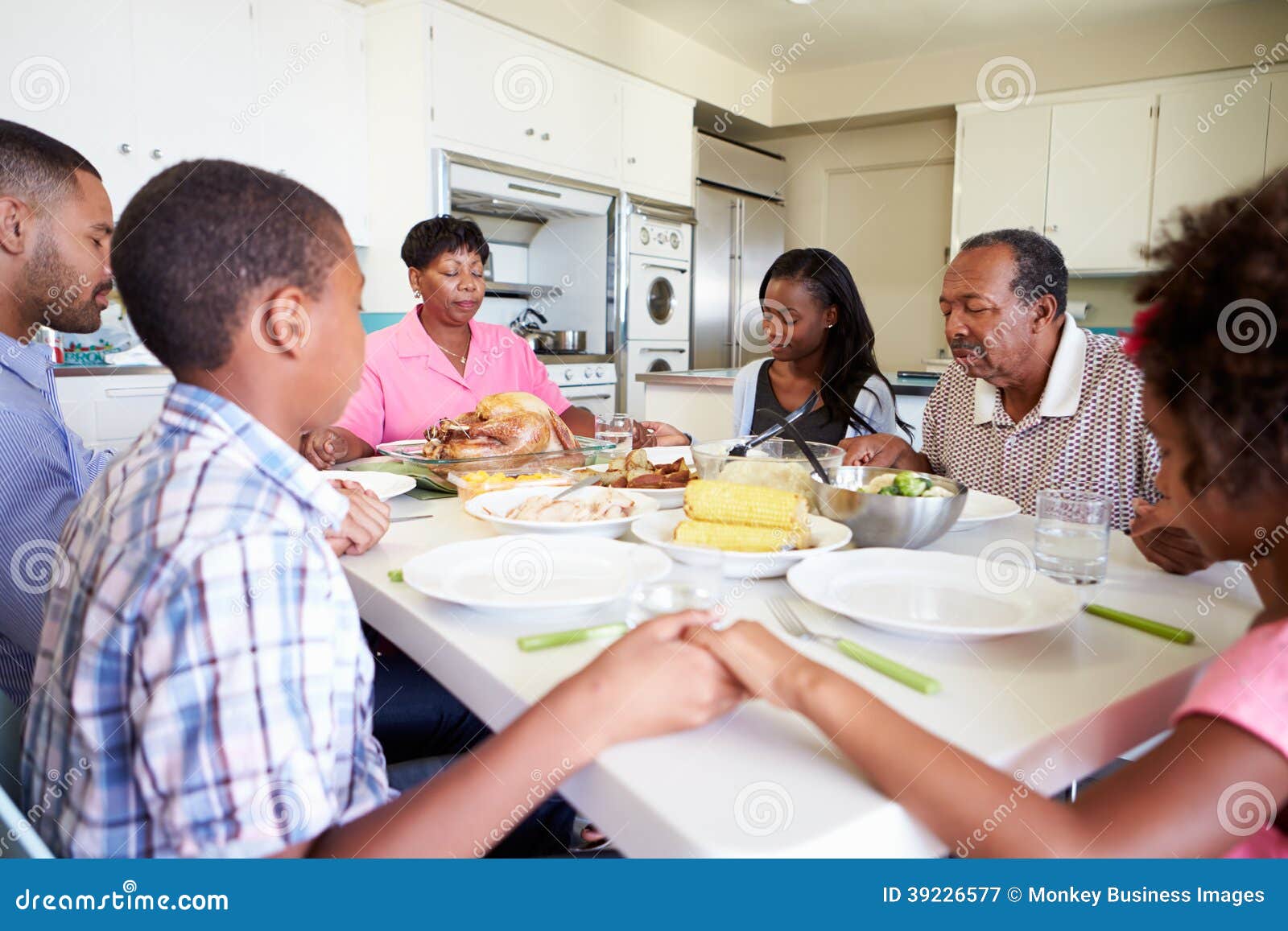 multi-generation family saying prayer before eating meal