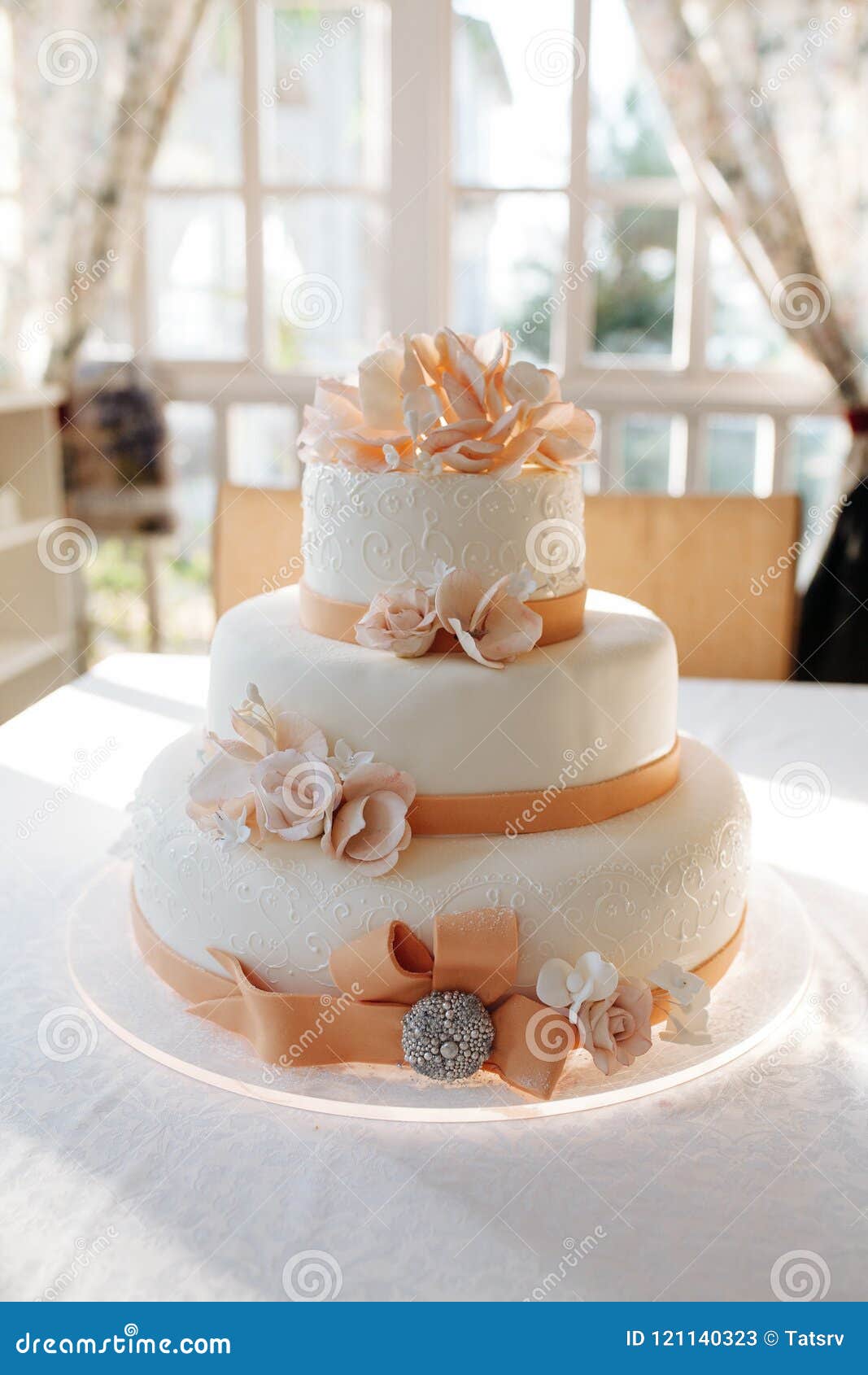 A Multi Level White Wedding Cake On White Table And Pink Flowers