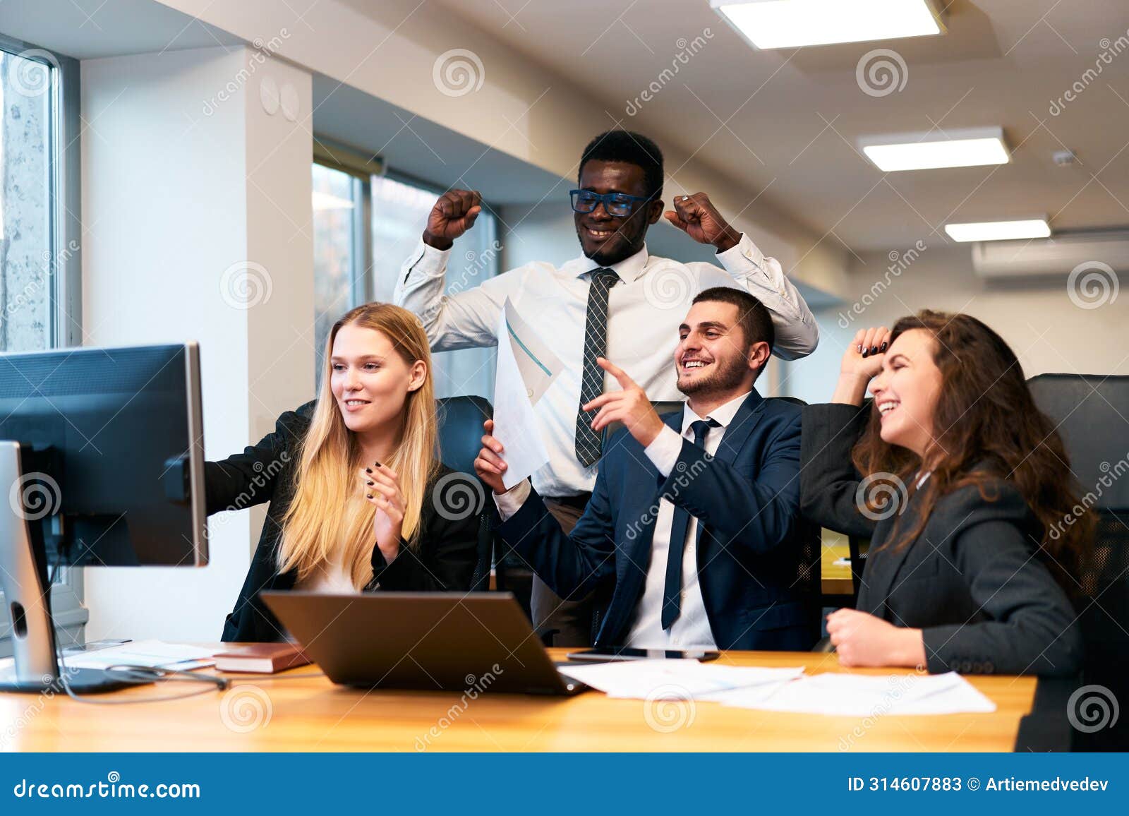 multiethnic office team rejoices around computer, happy african exec raises fists in victory, coworkers cheer, man