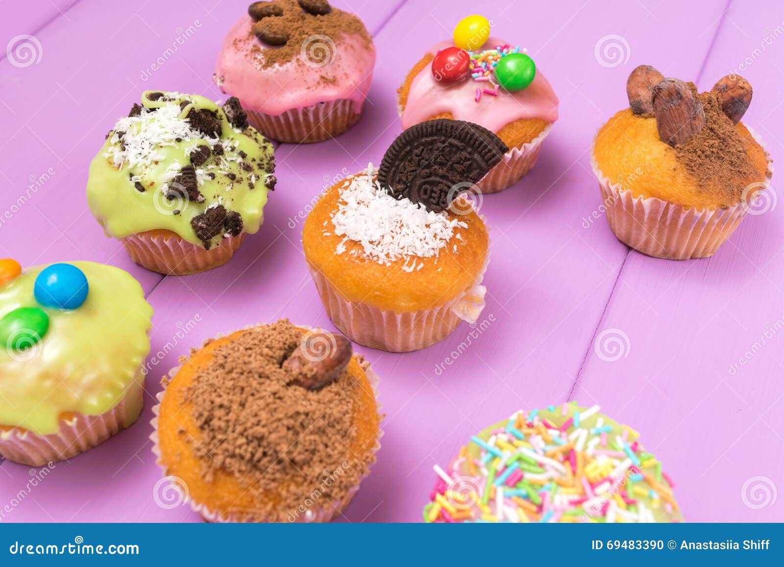 multiple muffins decorated with multicolored frosting, cocoa powder and beans, candies top view toned selective focus